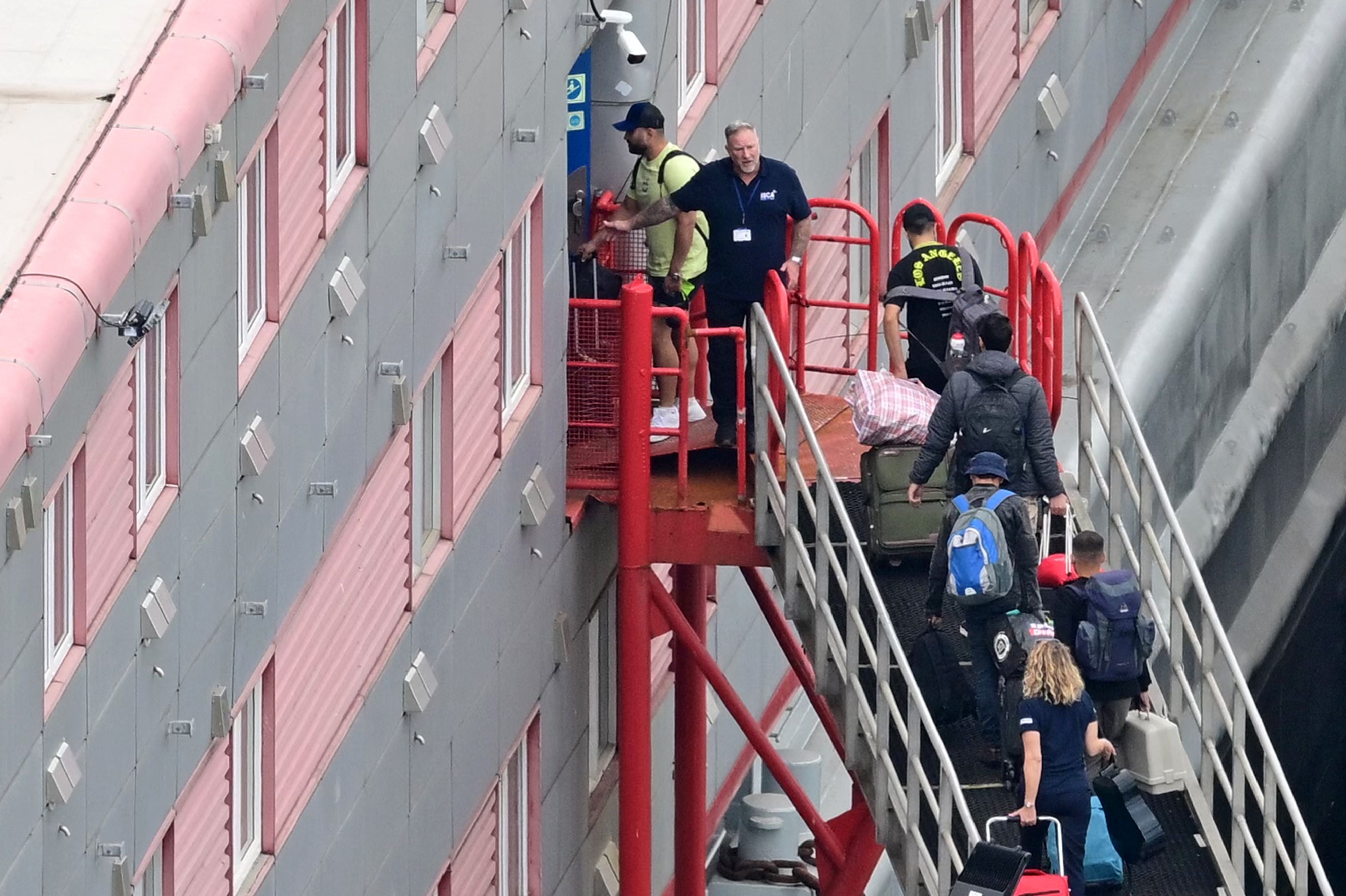 People carrying bags are seen walking up the gang-way into the Bibby Stockholm accommodation barge, moored to the quayside at Portland Port in Portland, on the south-west coast of England on August 7