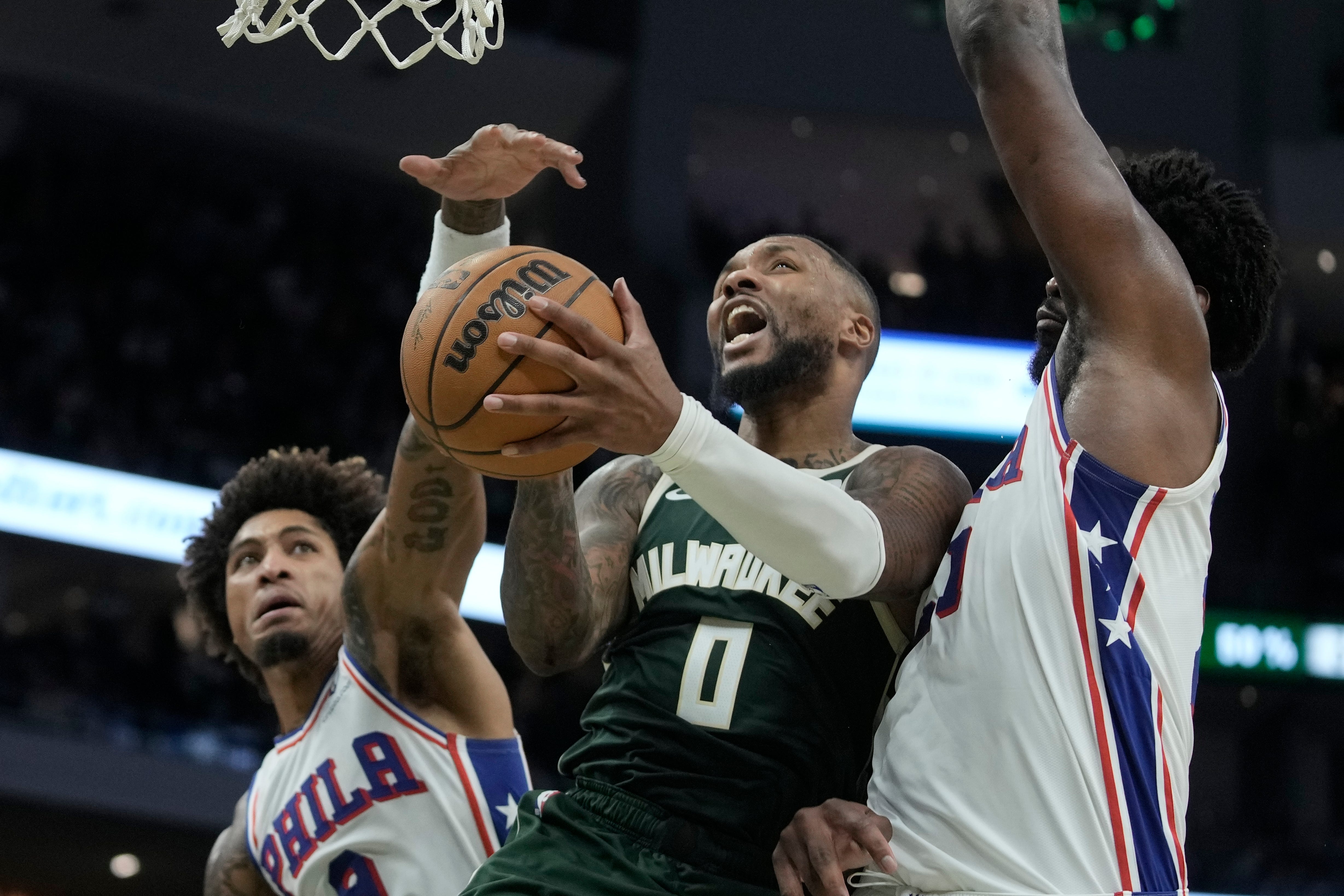 Milwaukee Bucks’ Damian Lillard shoots between Philadelphia 76ers’ Kelly Oubre Jr and Joel Embiid (Morry Gash/AP)