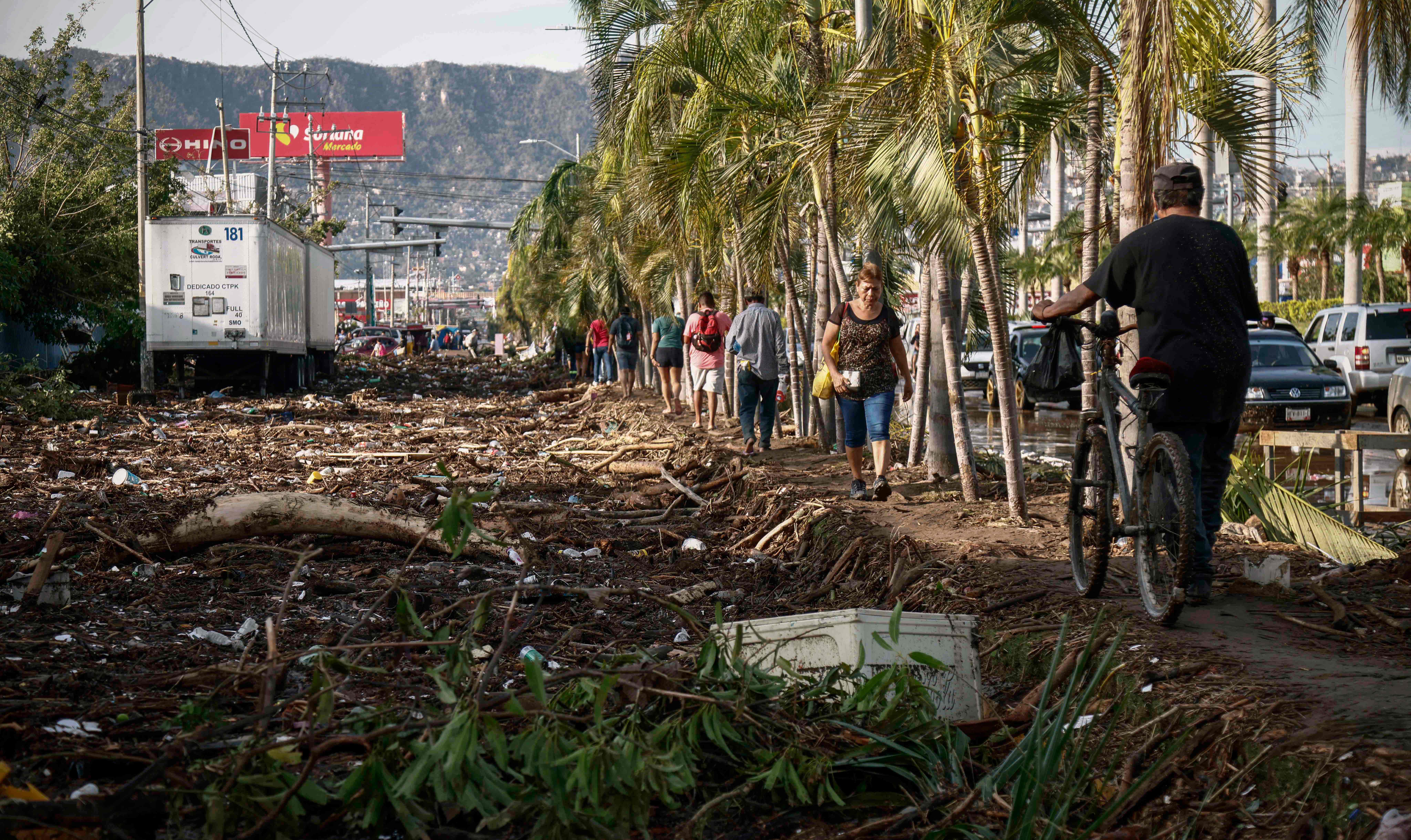 People walk next to debris left after the passage of Hurricane Otis in Acapulco