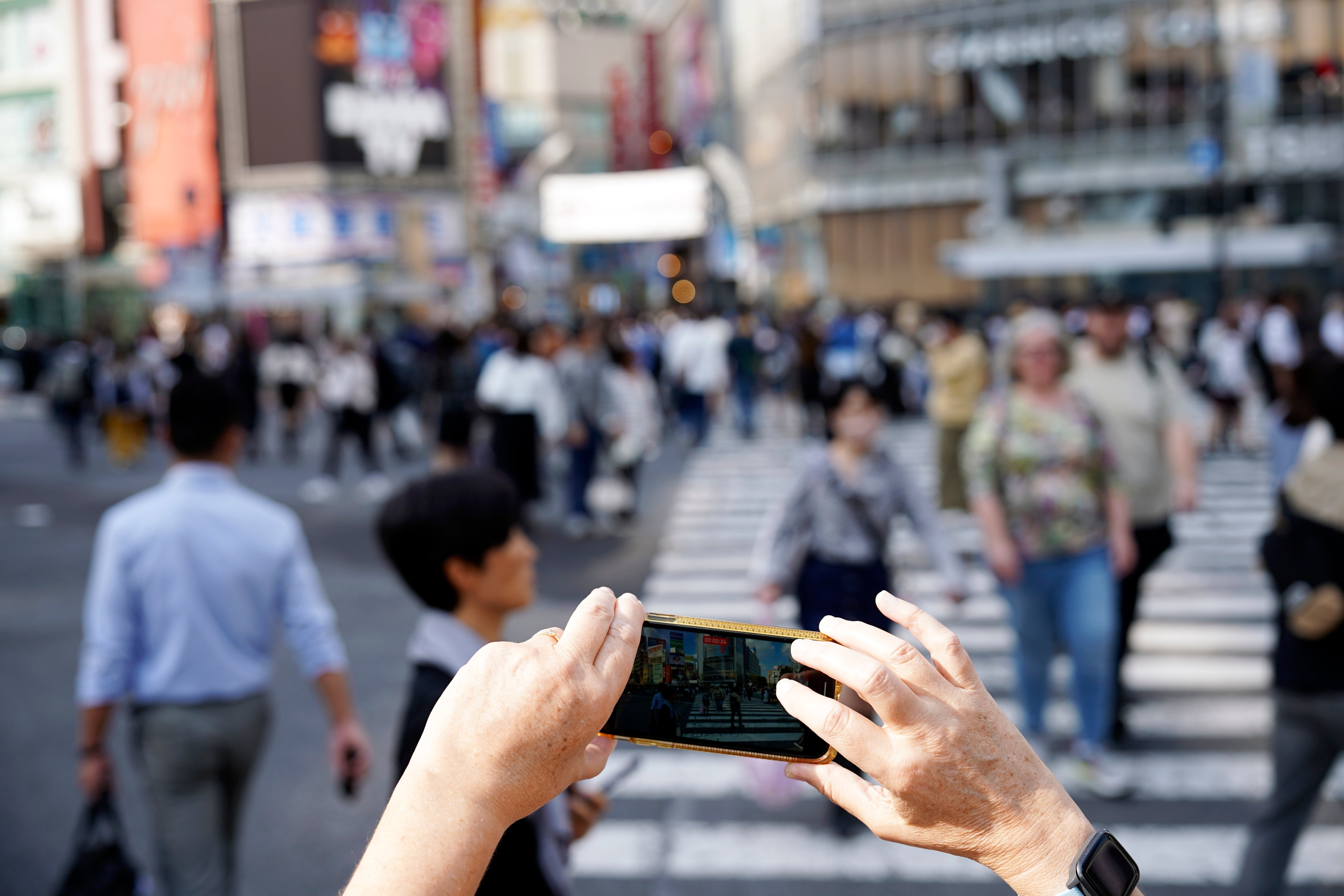 A foreign visitor films video with a mobile phone at the busy Shibuya pedestrian crossing in Tokyo