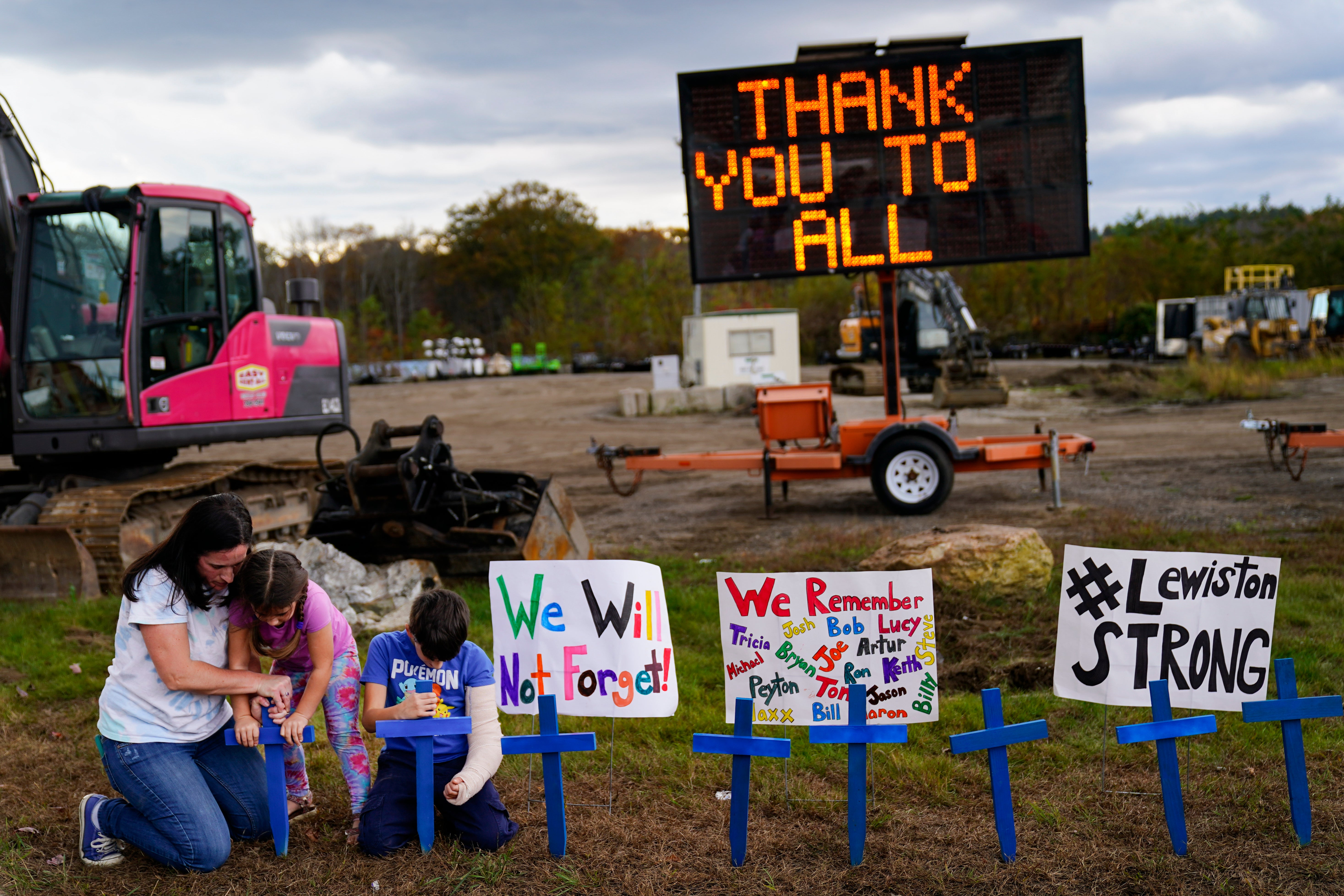 A family sit in front of signs honouring the lives lost in Lewiston’s mass shooting