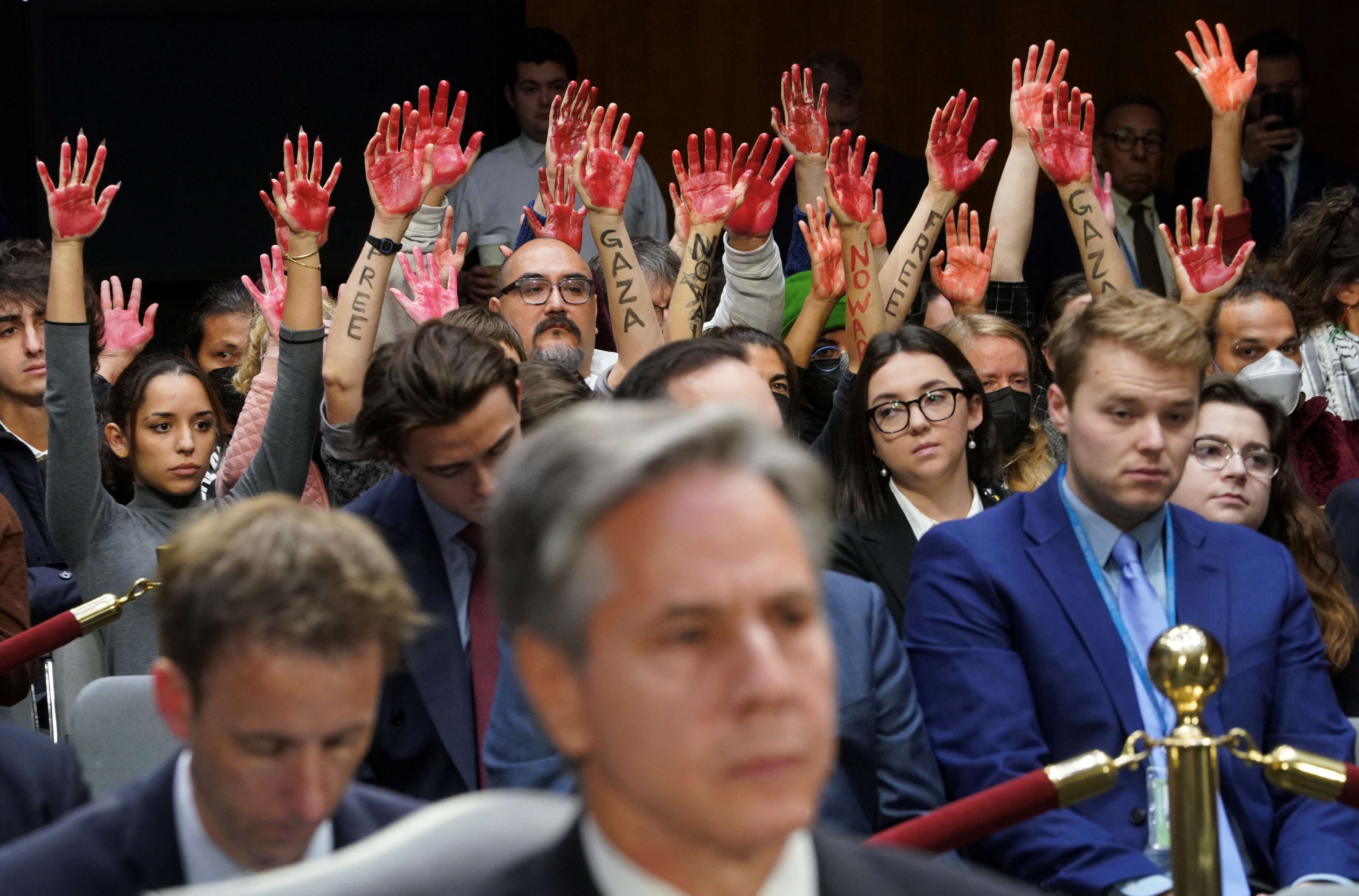 Anti-war protesters raise their ‘bloody’ hands behind US secretary of state Antony Blinken during a committee hearing on Biden's $105bn supplemental funding request to support Israel and Ukraine