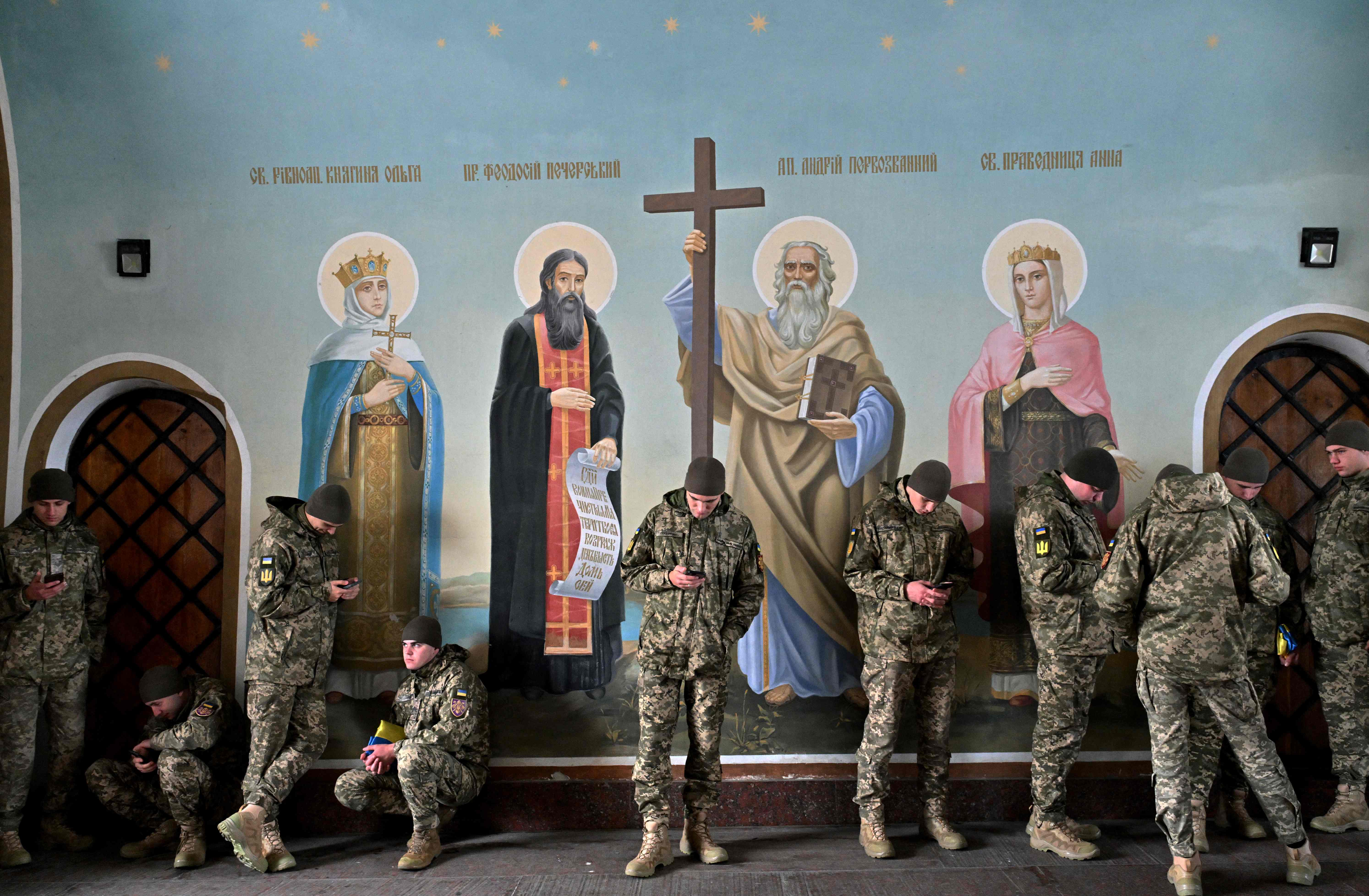 Ukrainian servicemen look at their phones as they shelter from the rain in St Michael’s Cathedral in Kyiv