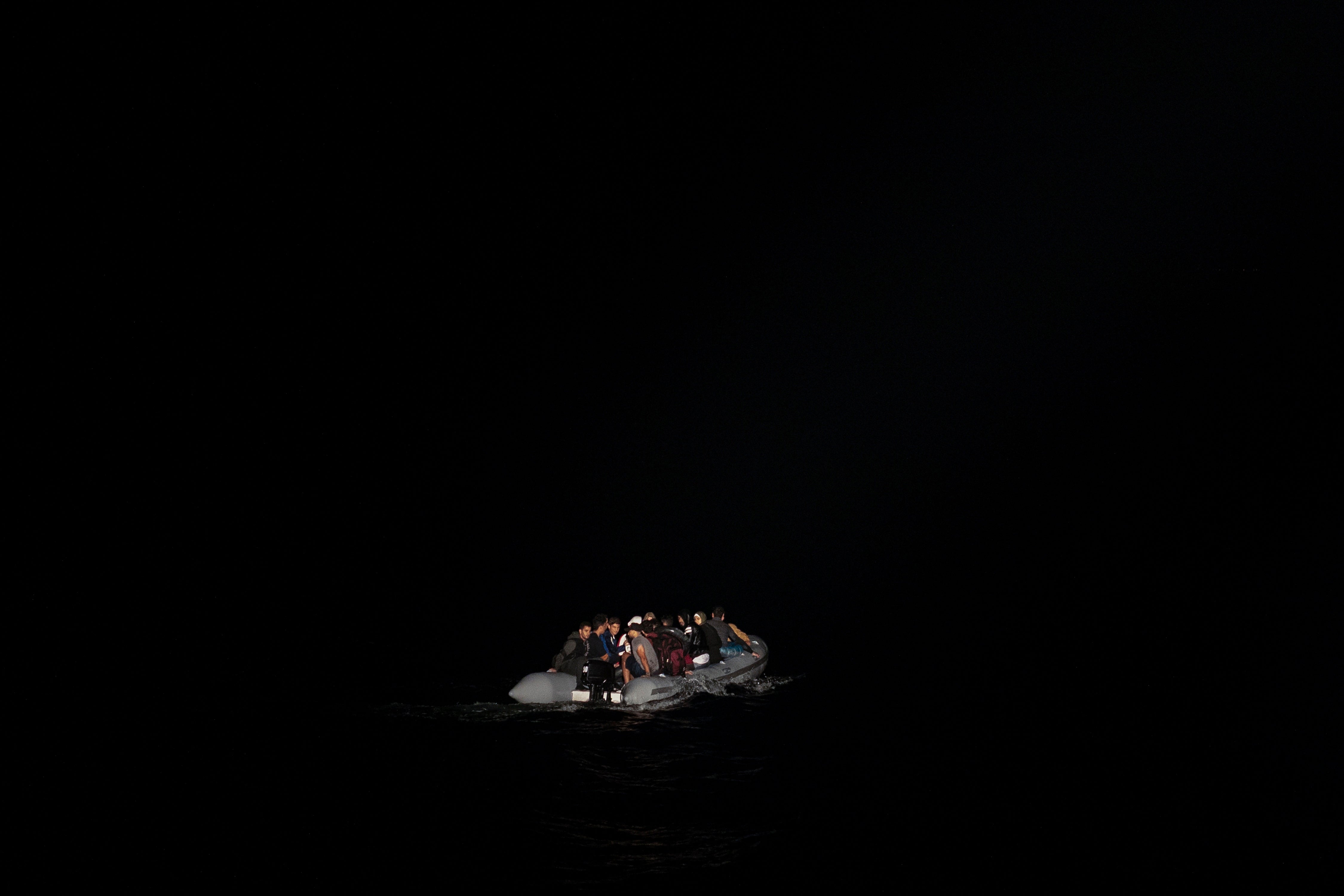 Refugees in a dinghy are lit by a a Greek coast guard patrol boat's spotlight during a rescue operation in 2019