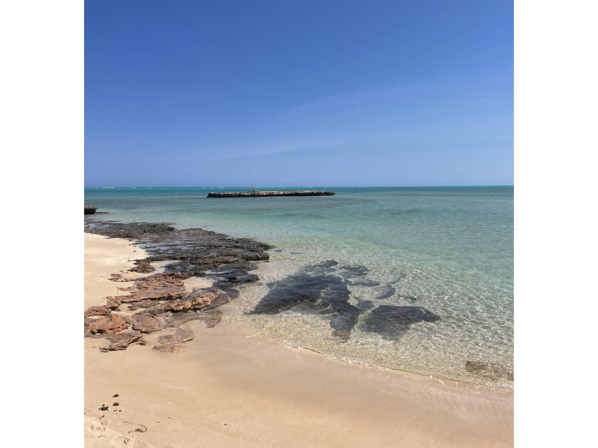 The aquamarine sea is backlit by bright, white sand