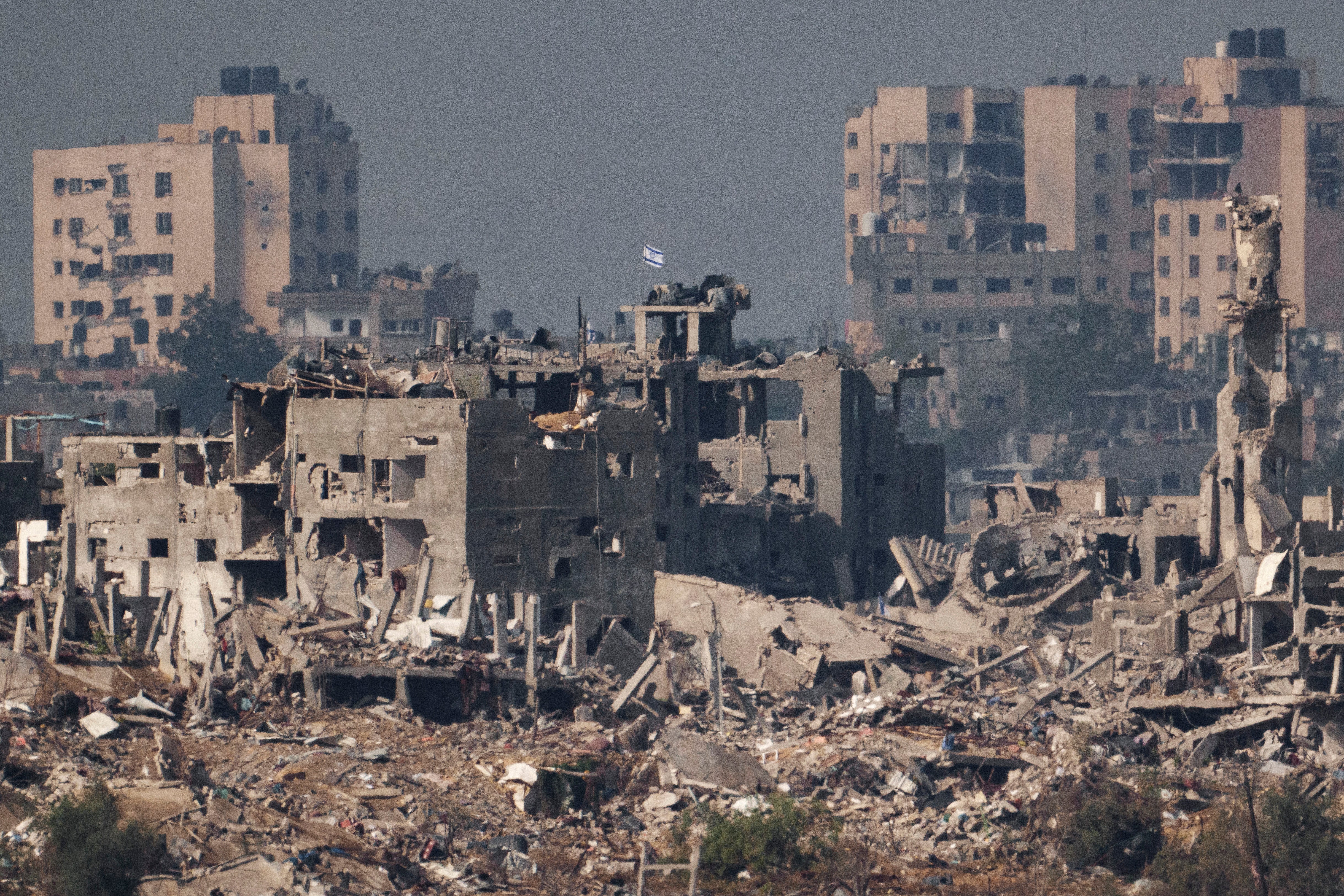 An Israeli flag stands above destroyed buildings in Gaza around a month into Israel’s siege of the region