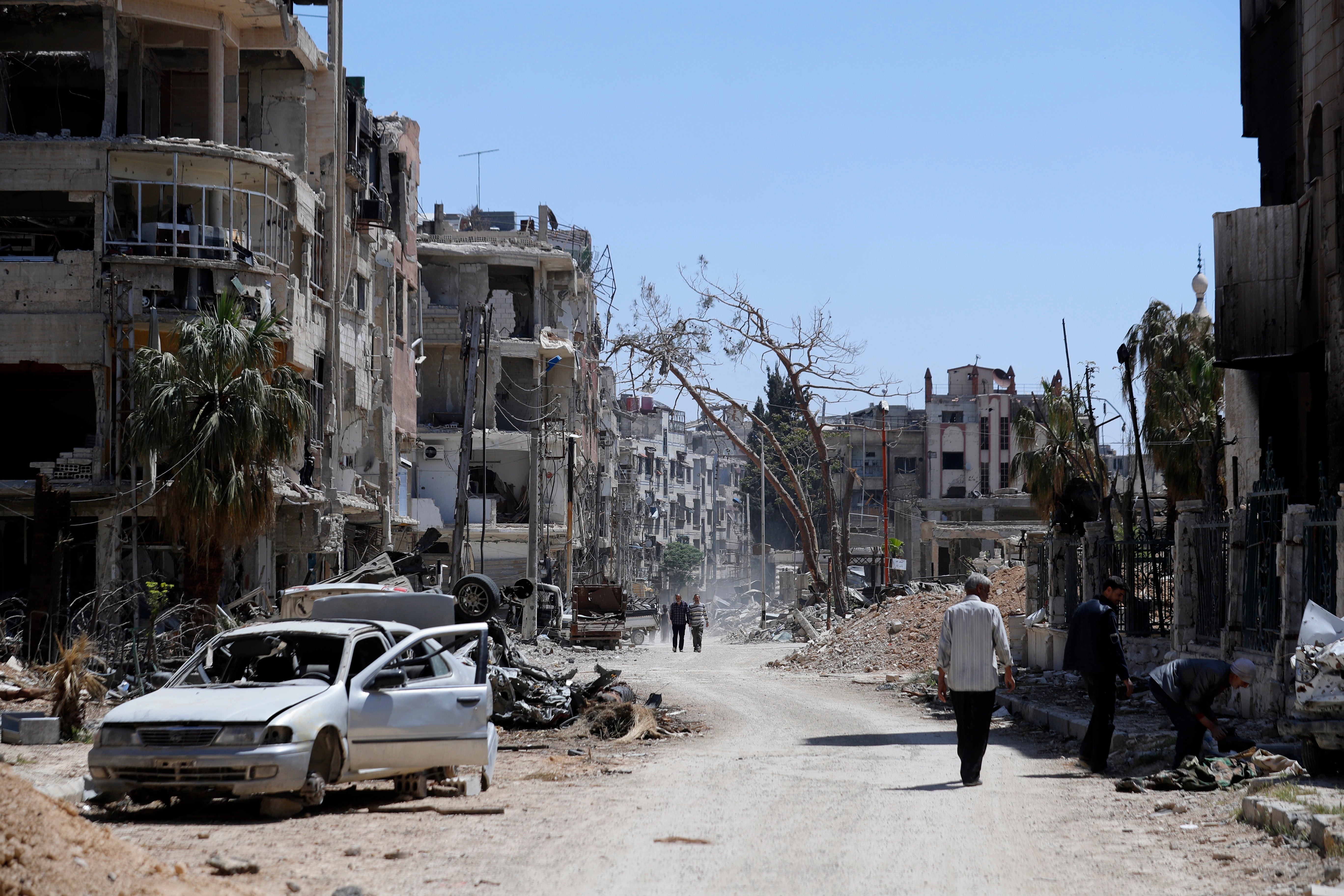 Syrians walk through destruction in the town of Douma, the site of a suspected chemical weapons attack, near Damascus, Syria