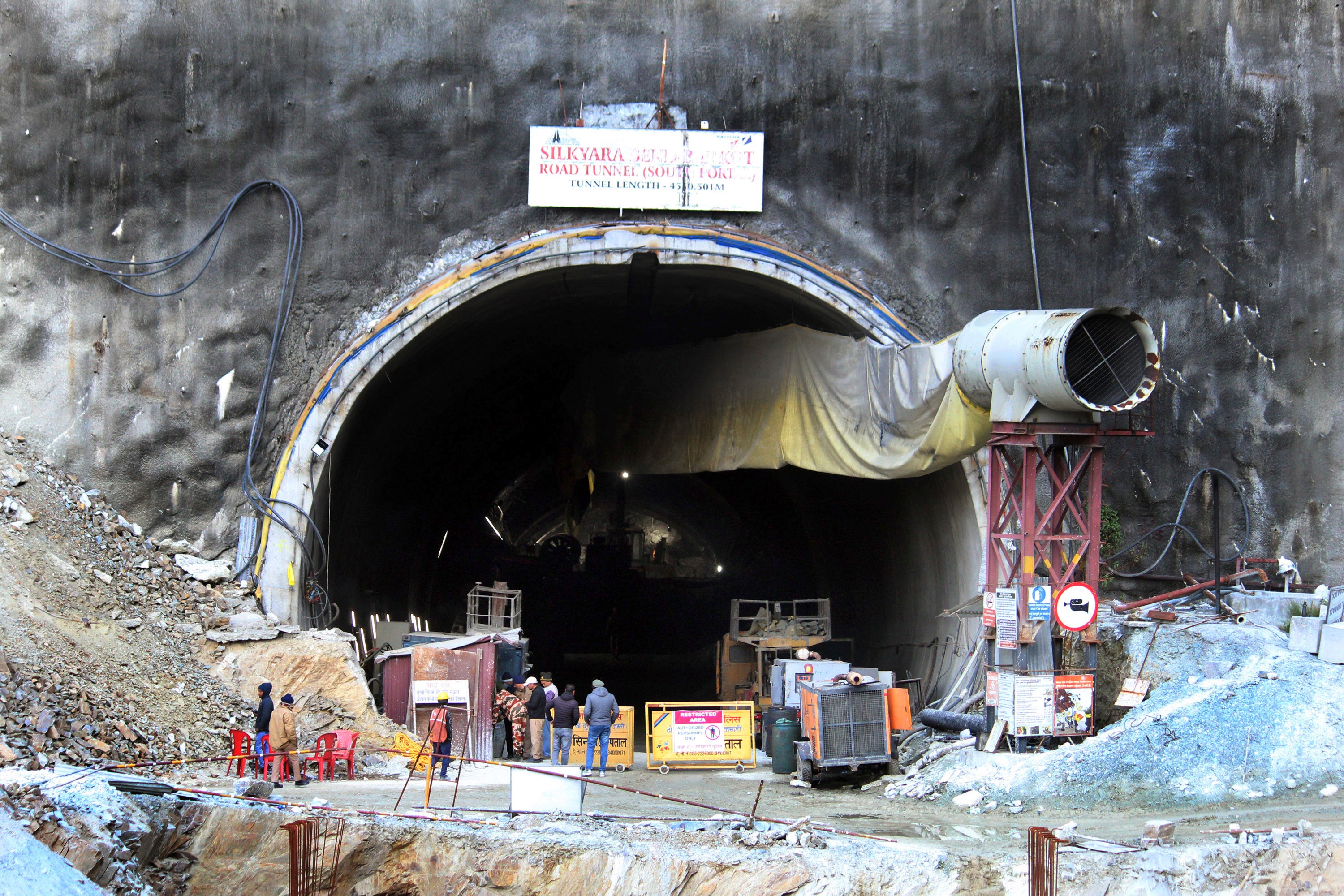 People stand near the entrance to the site of an under-construction road tunnel that collapsed in mountainous Uttarakhand state, India, Friday, 17 Nov 2023.