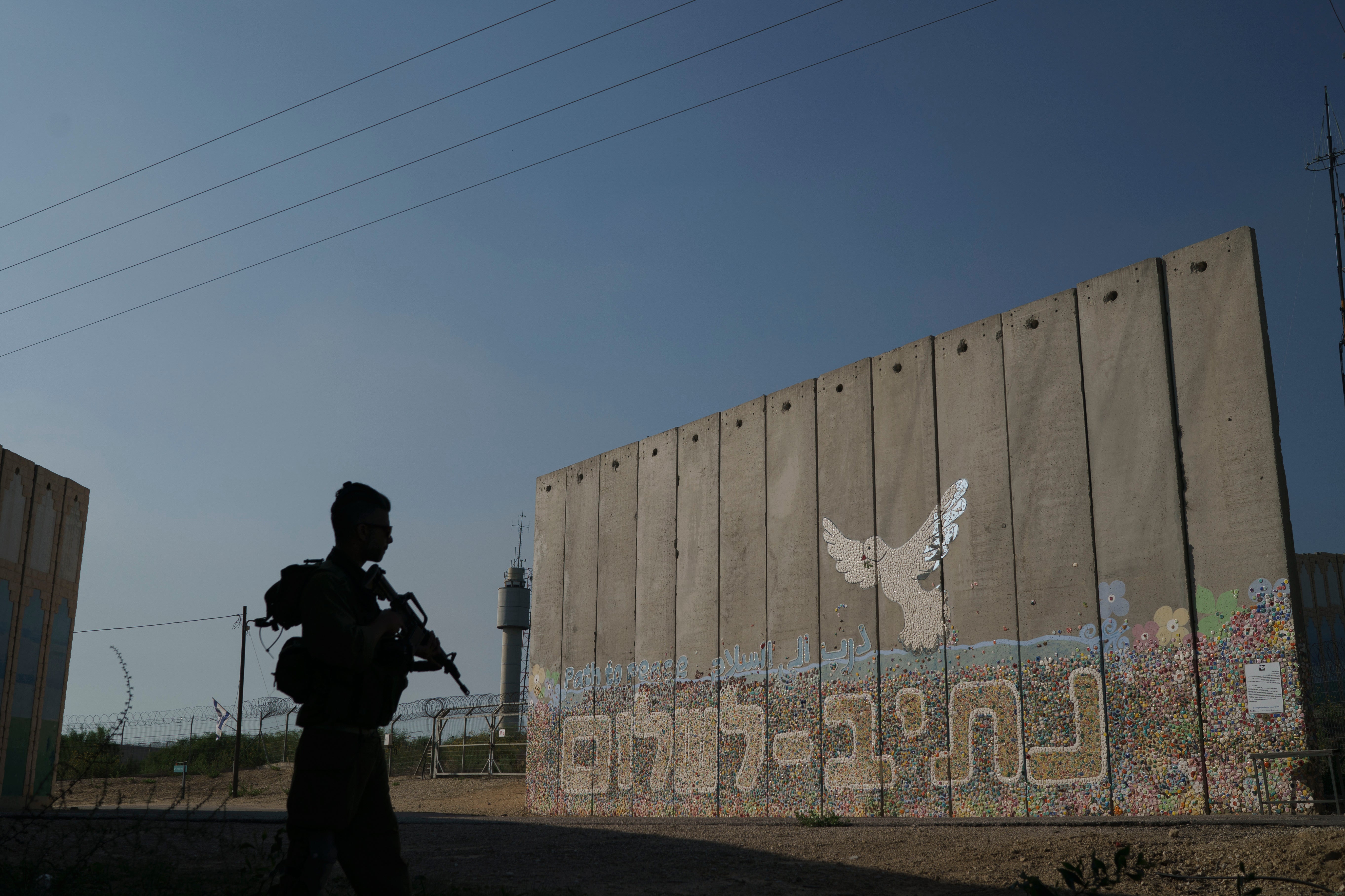 <p>A member of Israeli forces stands next to a security wall with Hebrew writing reading ‘Path to Peace’ at the Kibbutz Netiv HaAsara, near the border with Gaza Strip, in November 2023</p>