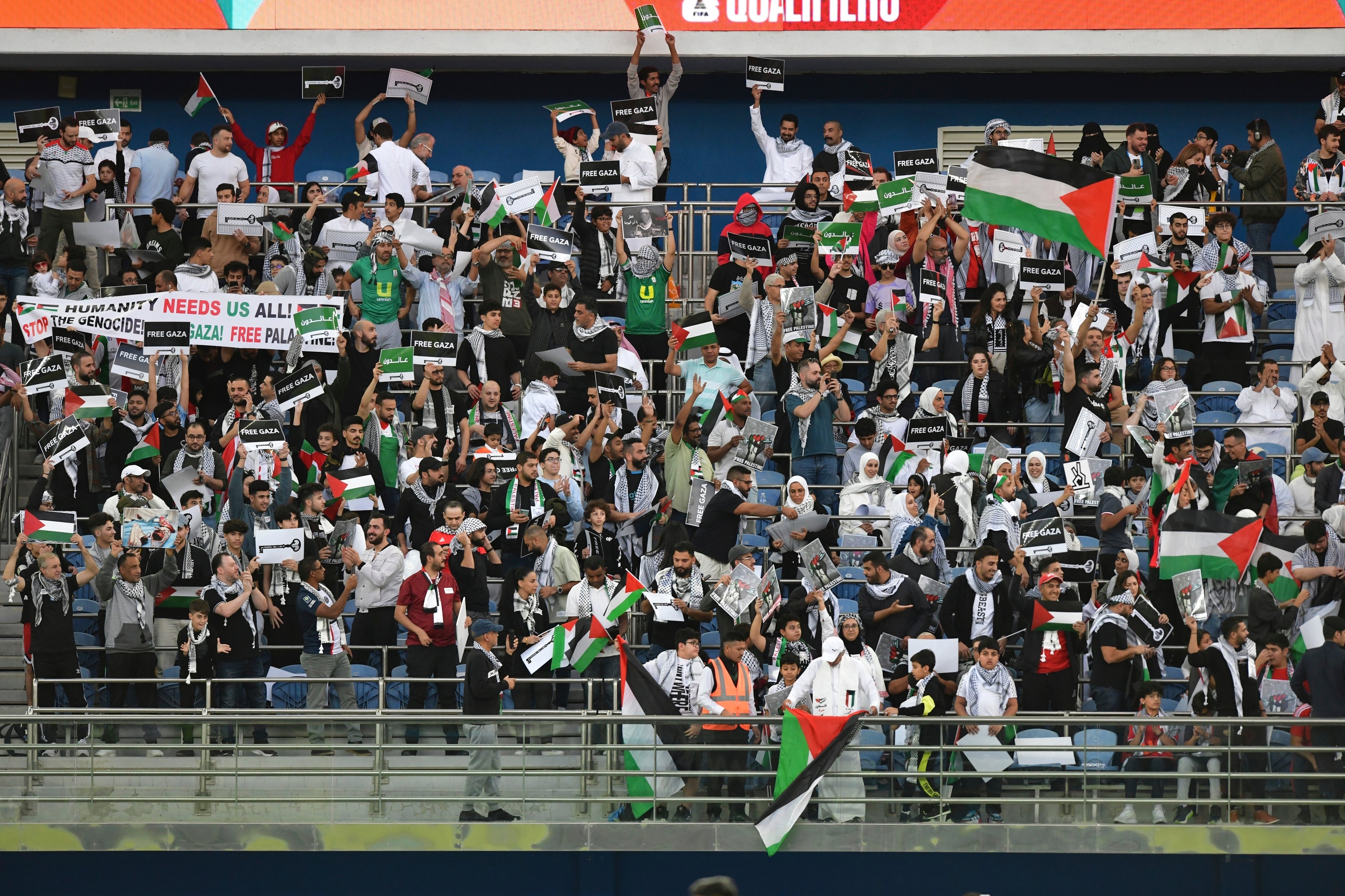 Palestinian fans wave Palestine national flags and hold pro Palestinian banners during a qualifying match