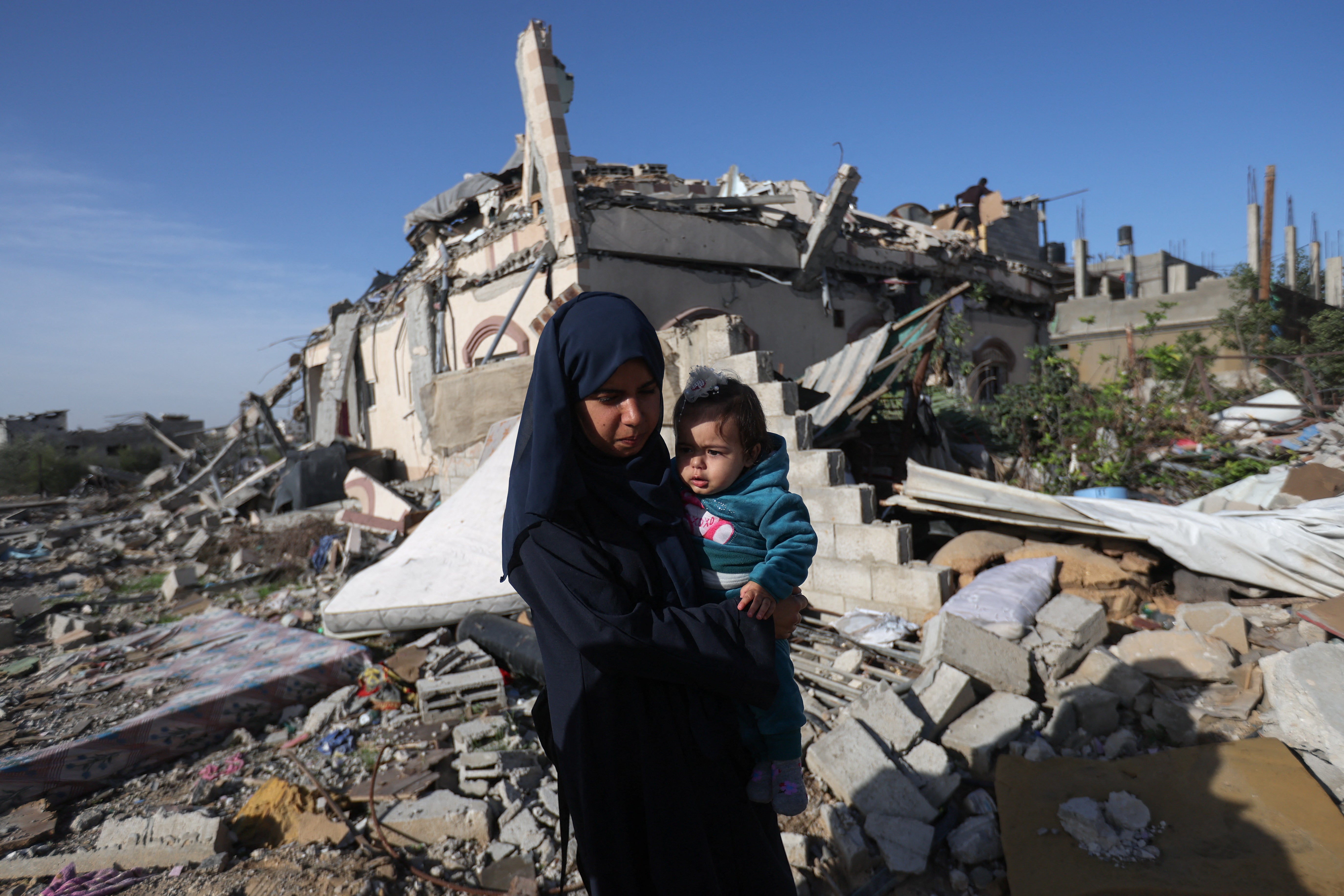 A Palestinian woman carries a child as she walks next to houses destroyed in an Israeli strike during the conflict, amid the temporary truce between Hamas and Israel