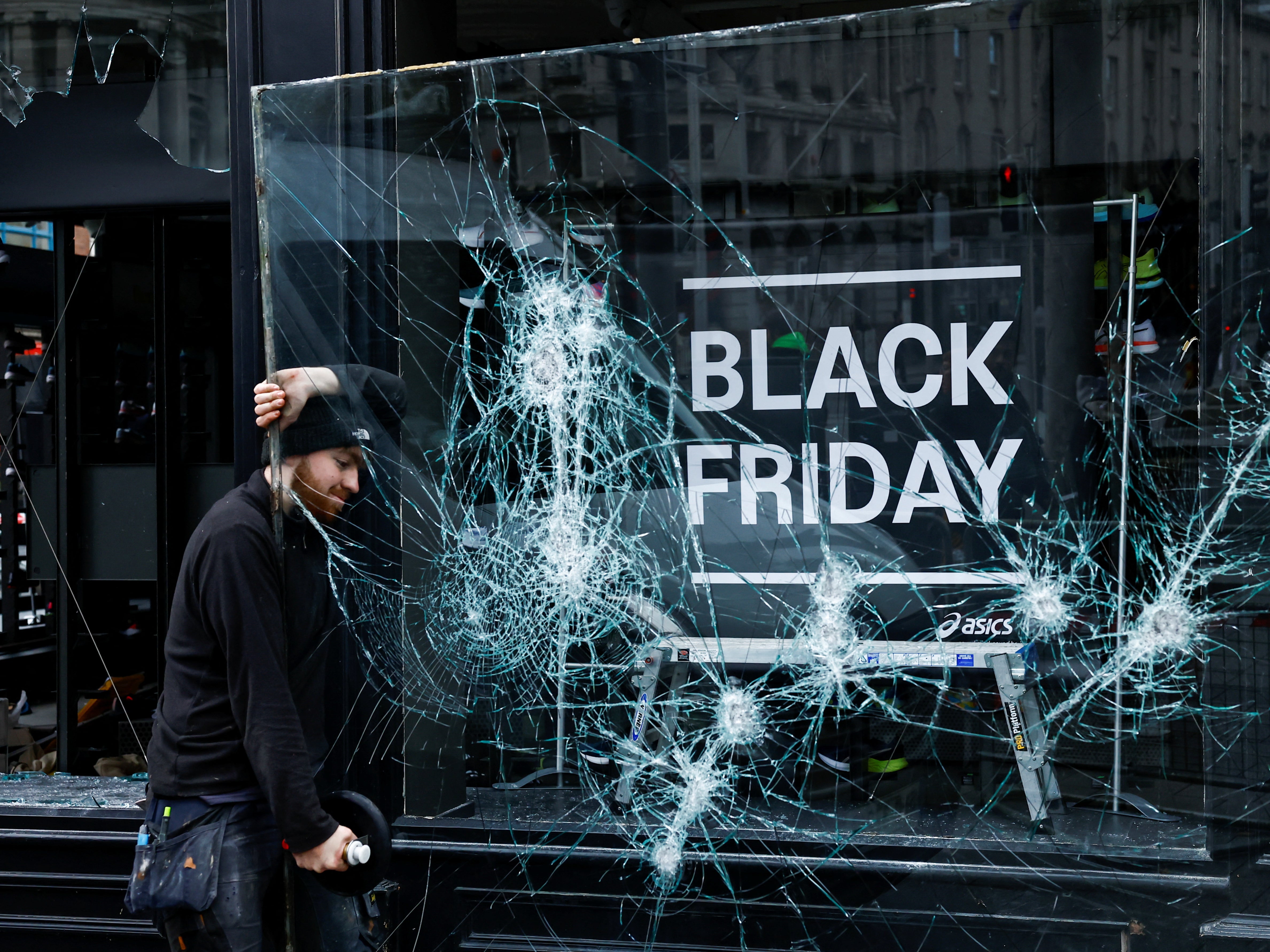 A man works to remove a broken window from a sport shop that was damaged in the riots