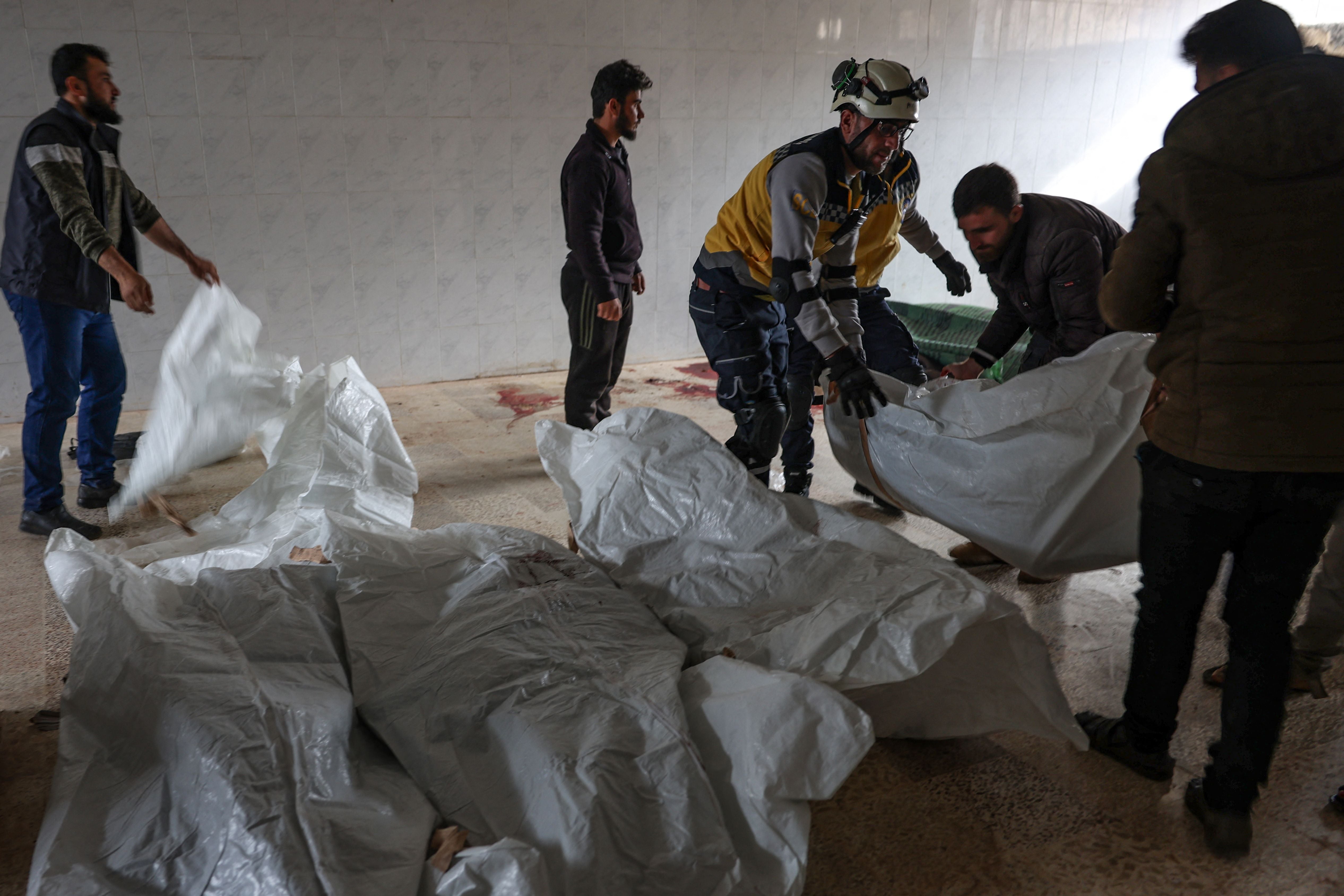 Residents and a rescuer from the Syrian White Helmets, pile up bodies of civilians killed in a Syrian regime bombardment in the town of Kaokafin in the rebel-held Idlib province on November 25, 2023