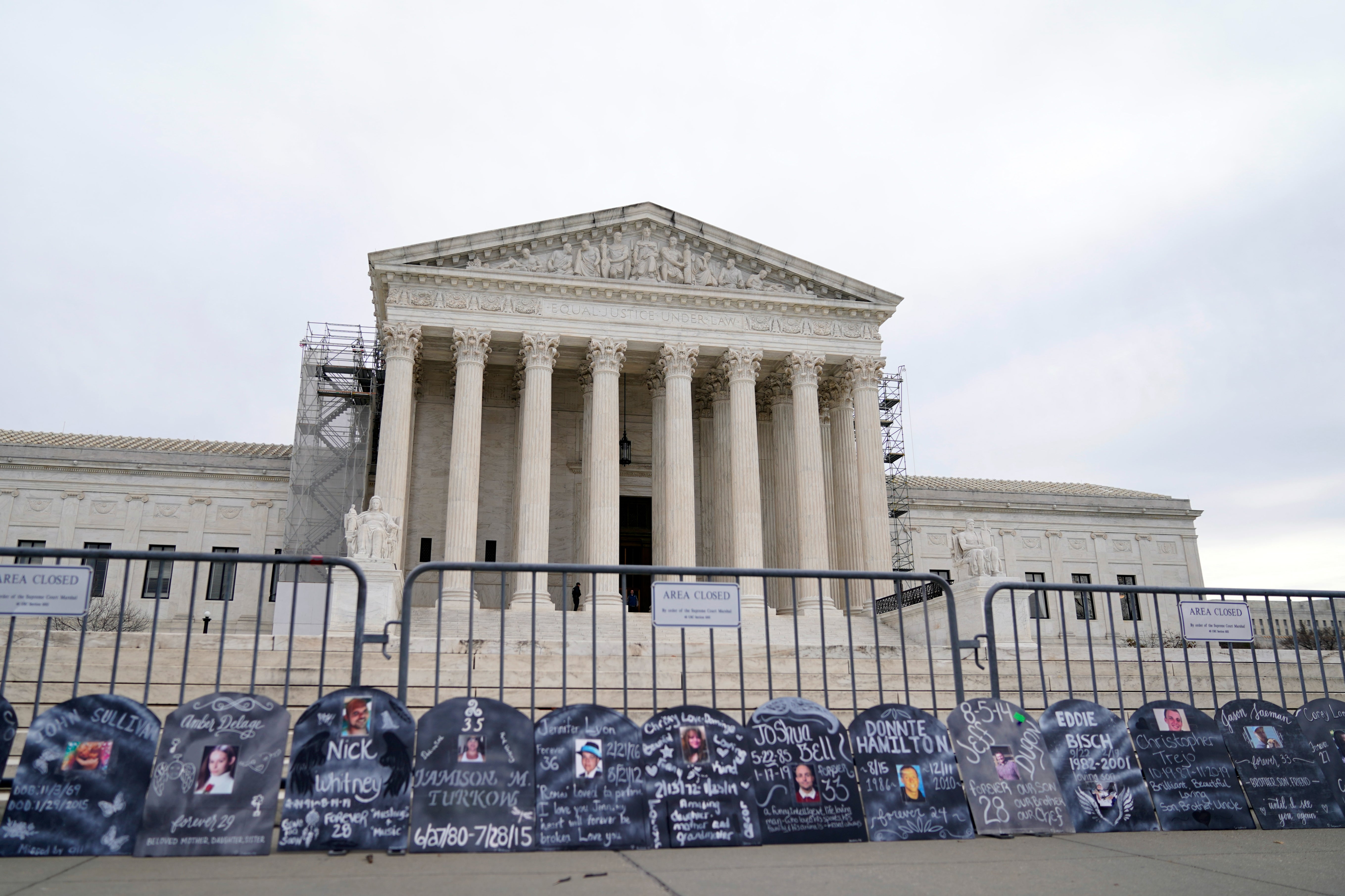 Signs in the shape of grave headstones, with information on people who died from using OxyContin, line a security fence outside the Supreme Court Monday, Dec. 4, 2023