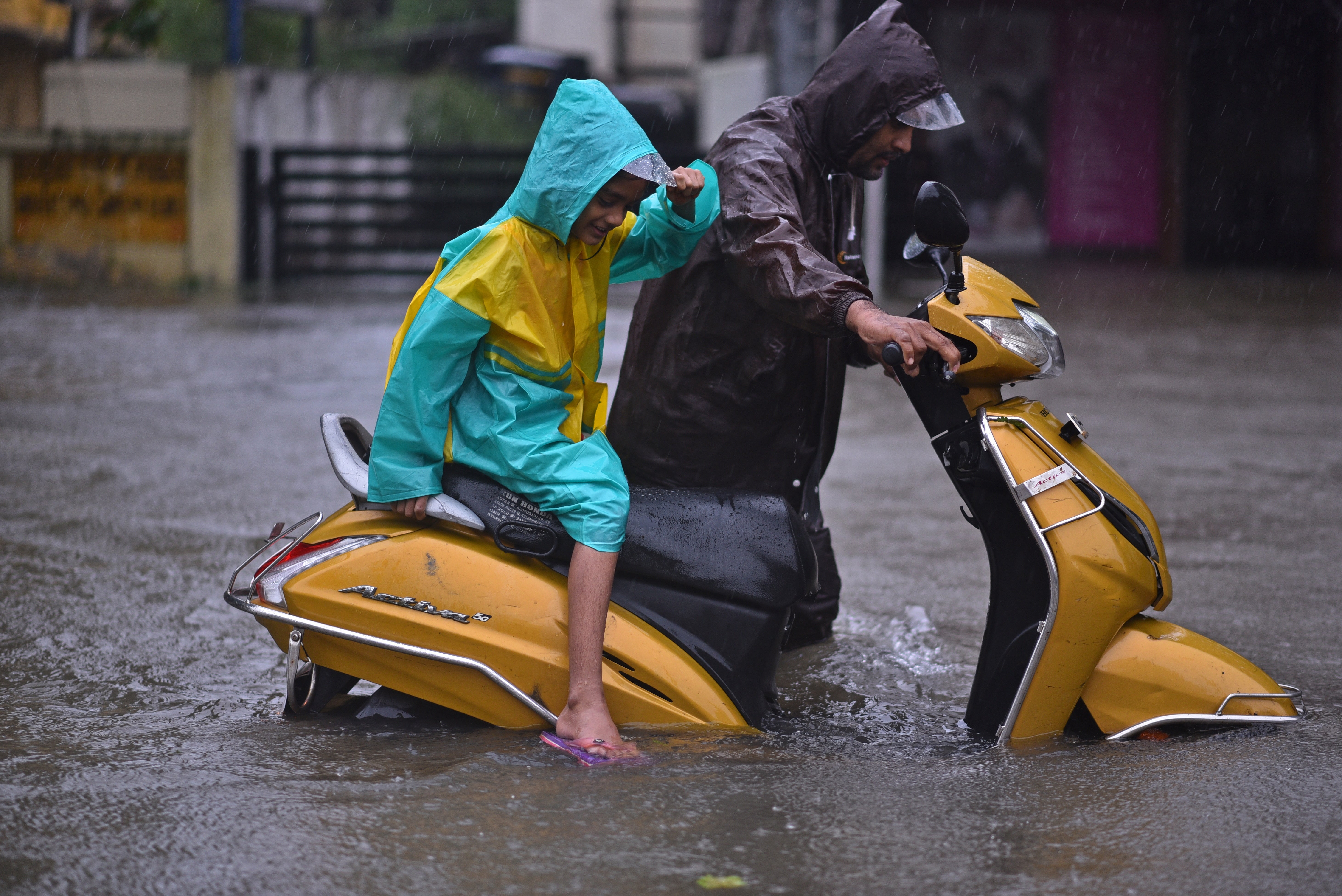 A man along with his daughter wades with his stalled vehicle on a flooded road during heavy rains as Cyclone Michaug makes landfall