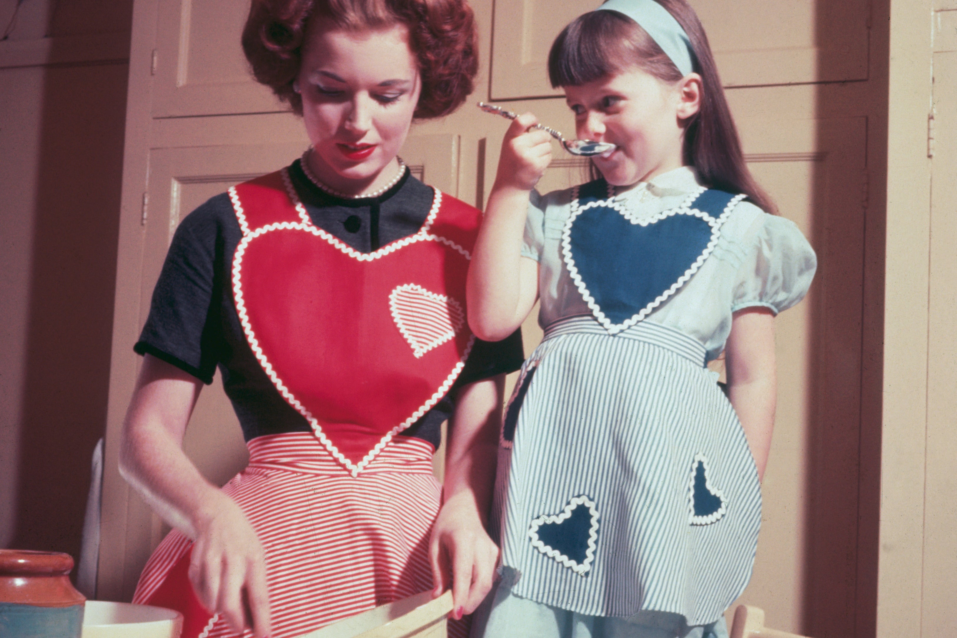 A young girl helps in the kitchen while her mother bakes a cake, circa 1955