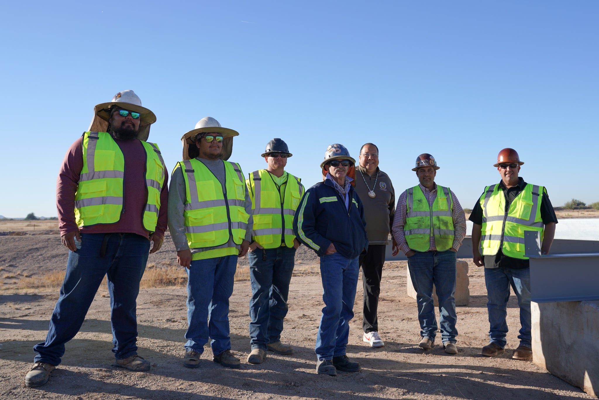 Governor Lewis stands with several people in hard hats and high-visibility vests at the 8 December ground-breaking ceremony.