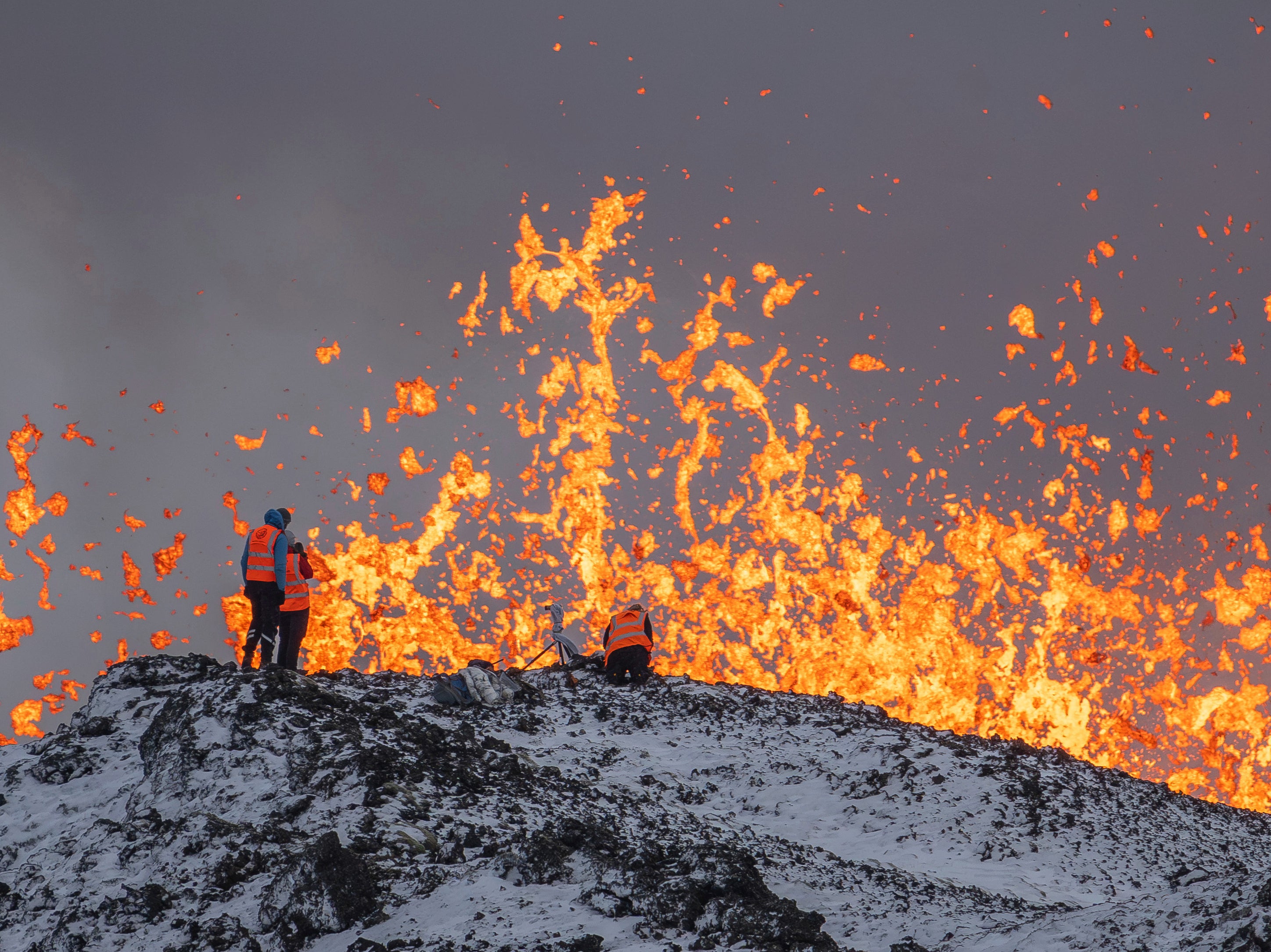 Scientist of the University of Iceland take measurements and samples standing on the ridge in front of the active part of the eruptive fissure of an active volcano in Grindavik