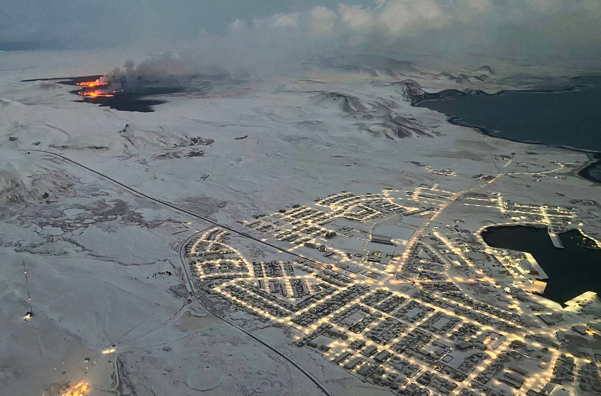 The evacuated Icelandic town of Grindavik (R) is seen as smoke billow and lava is thrown into the air from a fissure during a volcanic eruption on the Reykjanes peninsula 3 km north of Grindavik, western Iceland on December 19, 2023