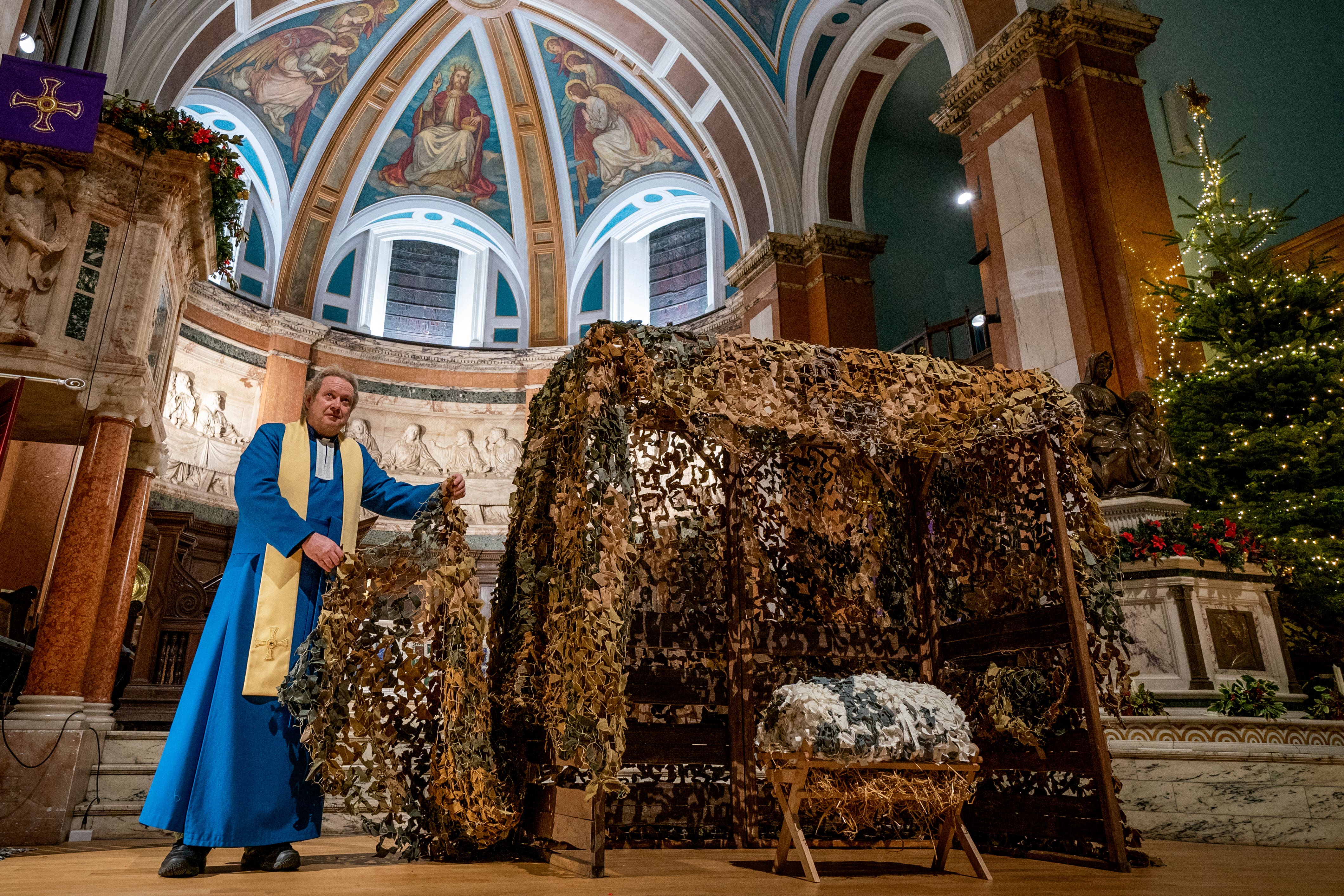 Parish minister Rev Peter Sutton stands alongside the Nativity scene in St Cuthbert’s Church, Edinburgh, which has been made using camouflage nets (Jane Barlow/PA)