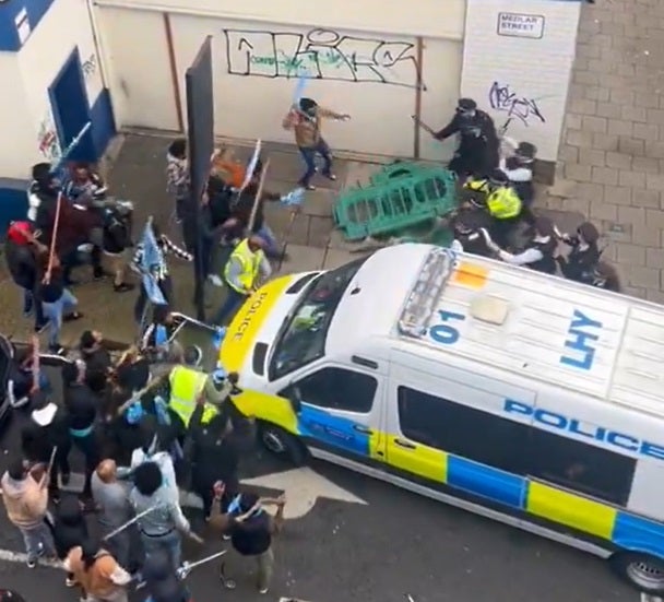 A barrier appears to be thrown at police officers by members of the public involved in the protest