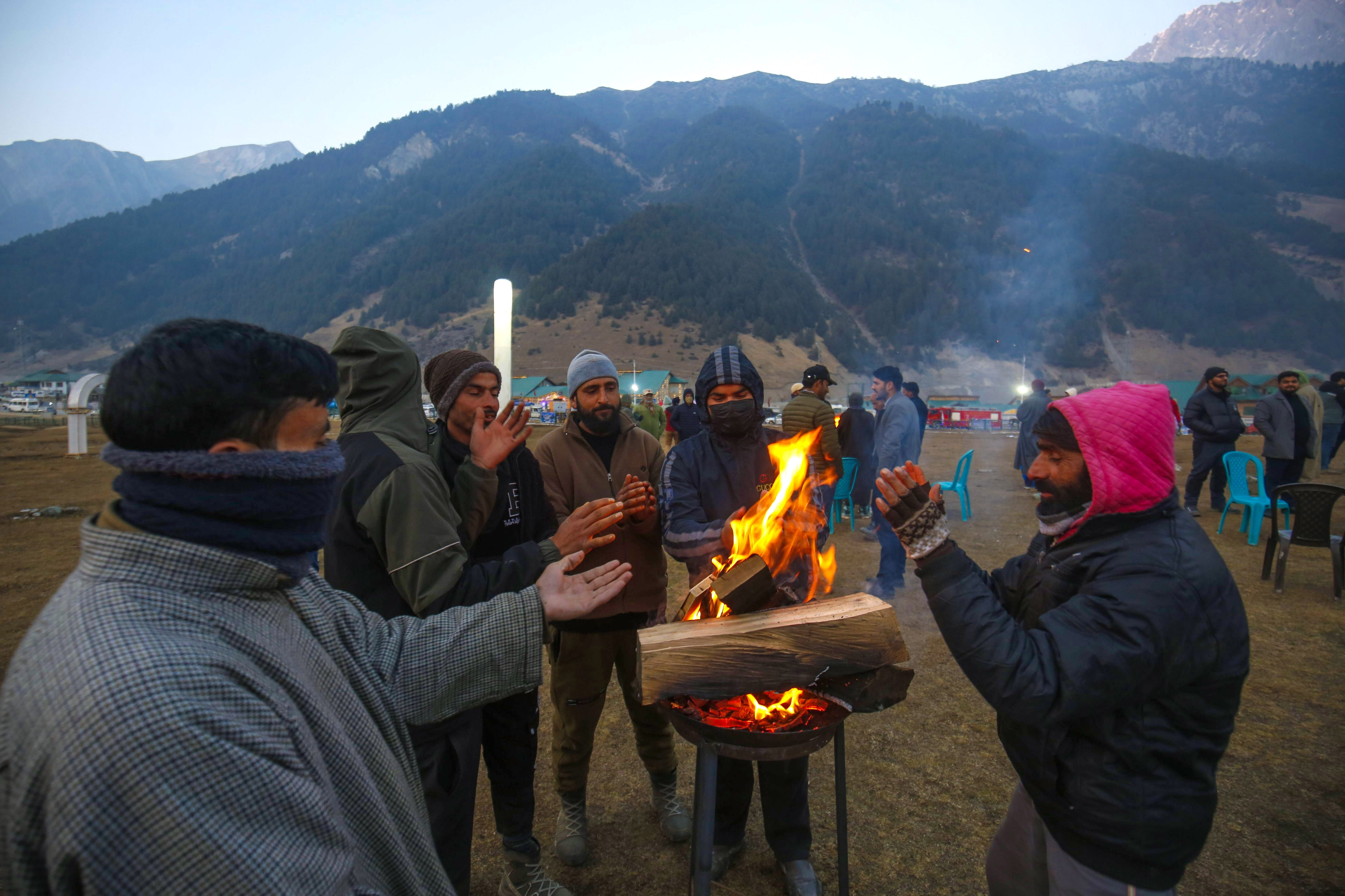 People warm themselves near a small fire as they attend the celebrations in Sonamarg, Indian Kashmir