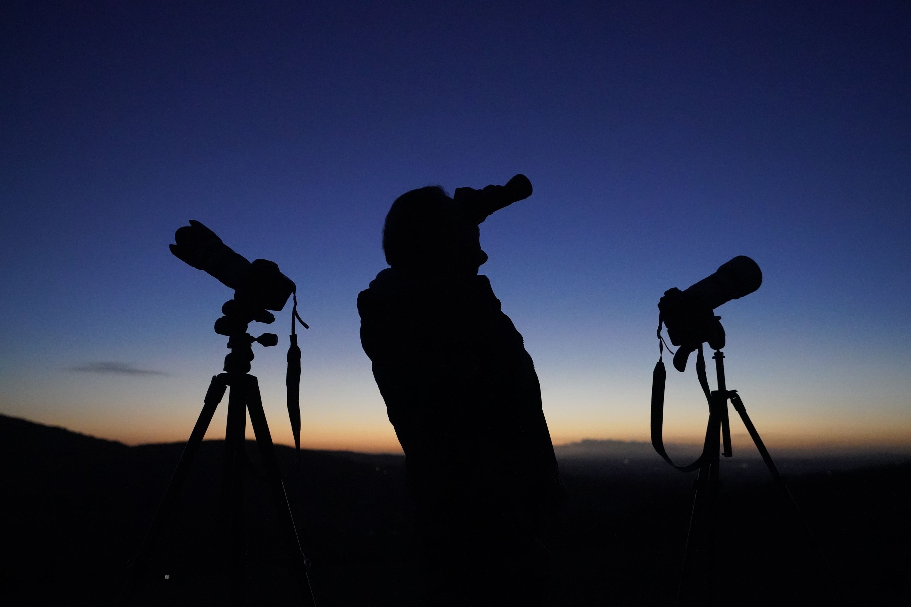 A man scours the night sky with binoculars and camera equipment from the Rock of Dunamase in Co Laois (Niall Carson/PA)