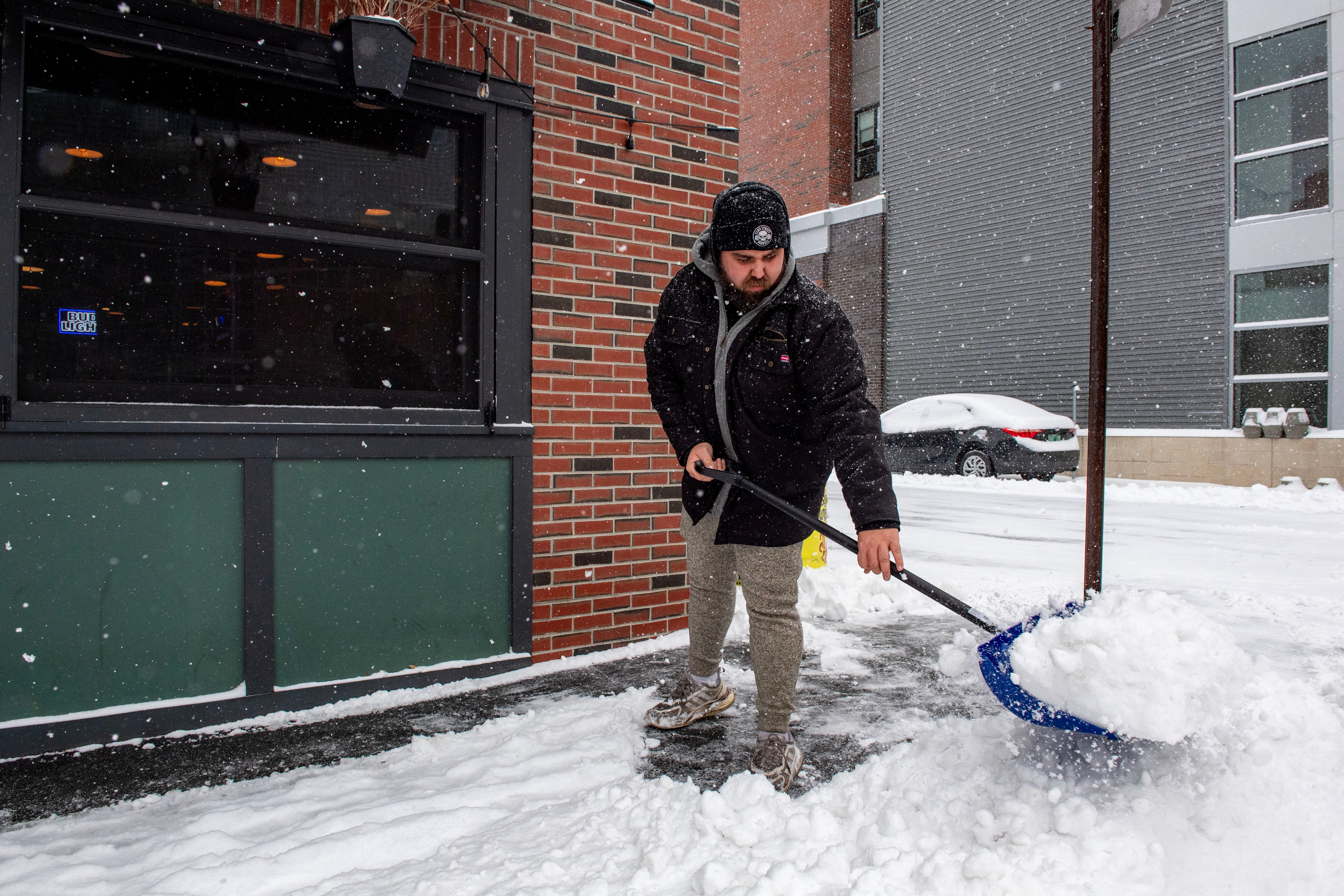 A person clears snow in front of a business in Manchester, New Hampshire