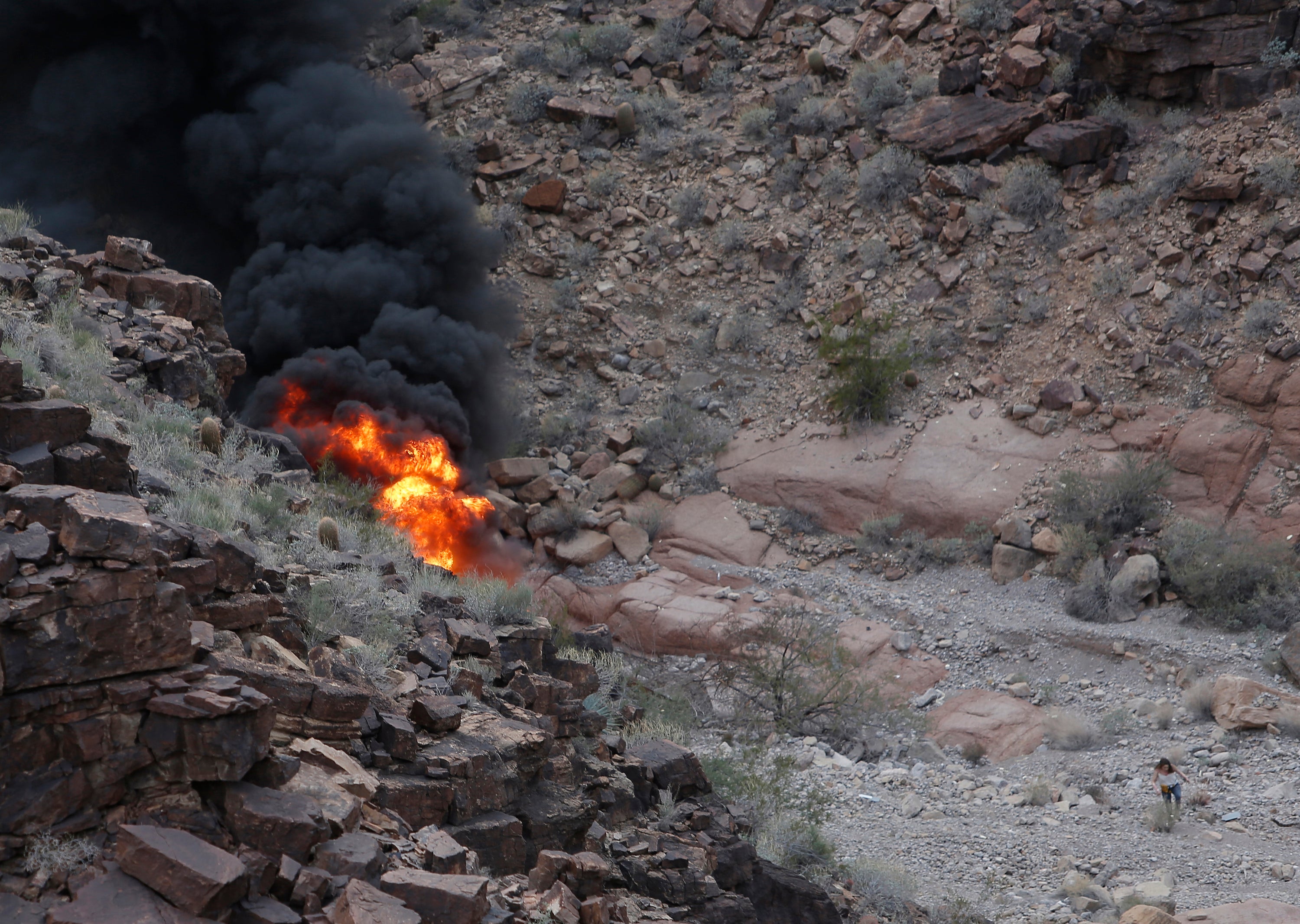 A survivor, lower right, walks away from the scene of the deadly tour helicopter crash along the jagged rocks of the Grand Canyon on February 10, 2018