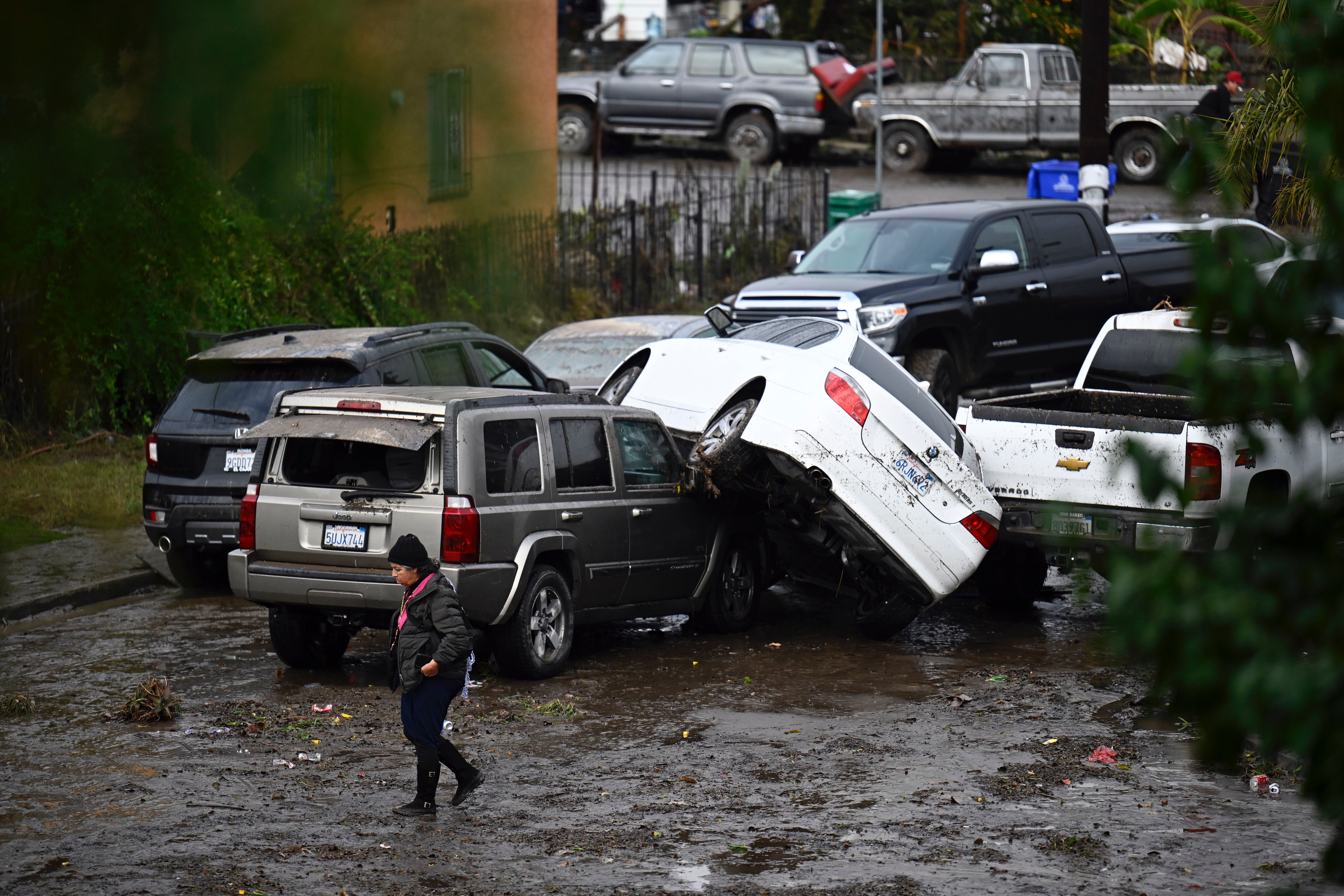 A woman walks by cars damaged by floods during a rainstorm in San Diego on 22 January, 2024