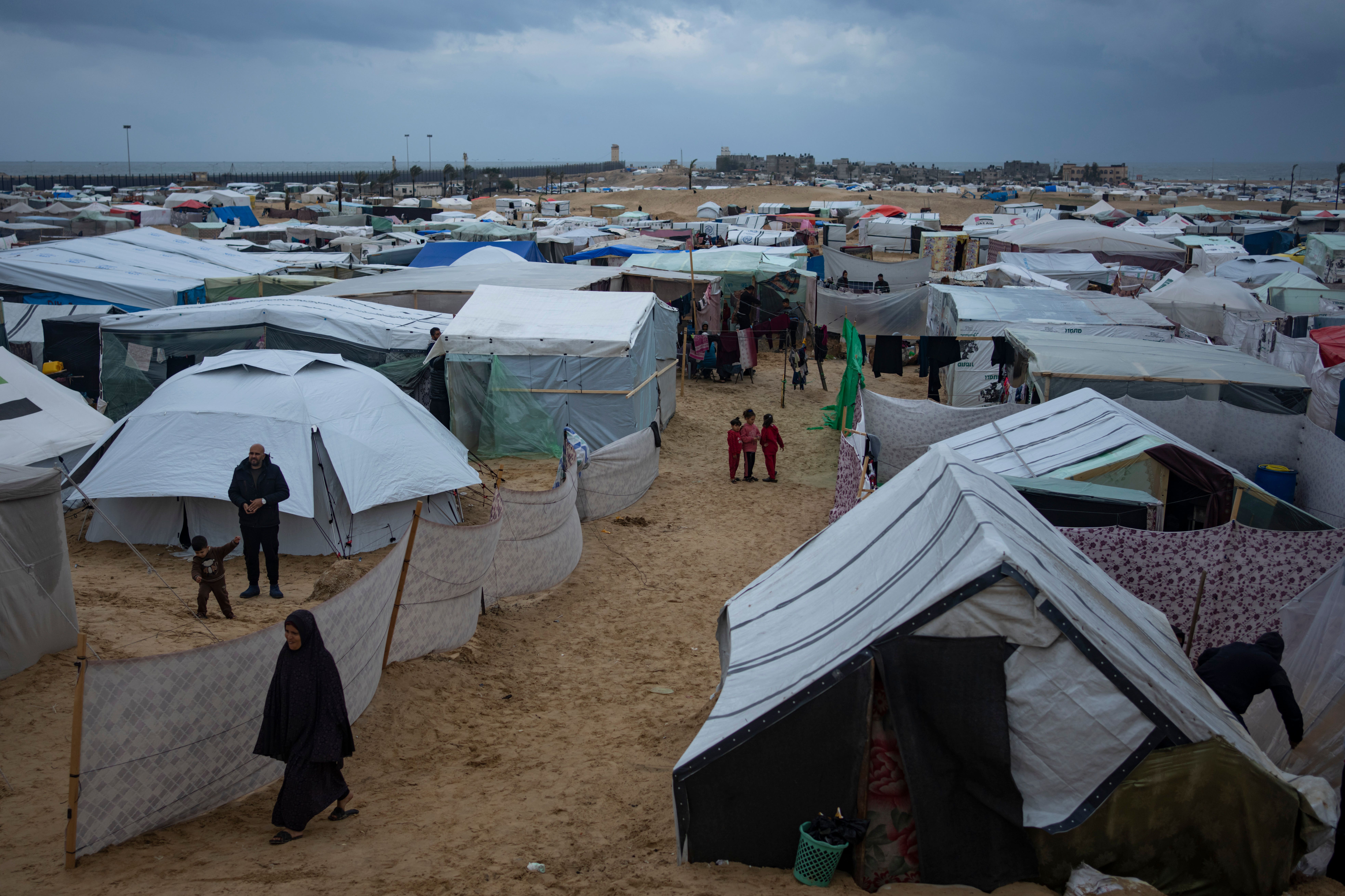 Palestinians displaced by the Israeli air and ground offensive on the Gaza Strip walk through a makeshift tent camp in Rafah (Fatima Shbair/AP)