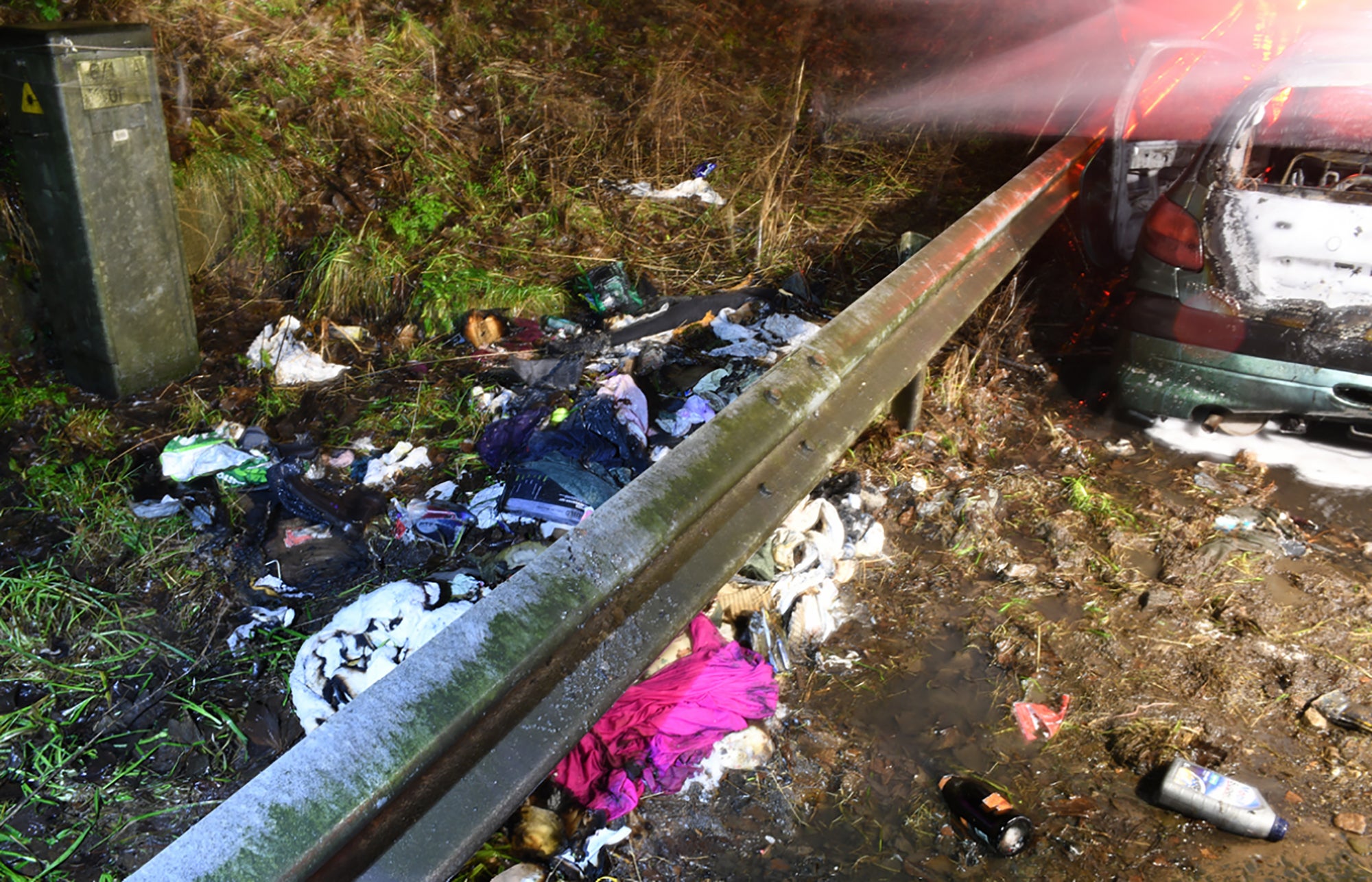 Tattered clothes and bottles lay strewn on the ground next to the destroyed vehicle