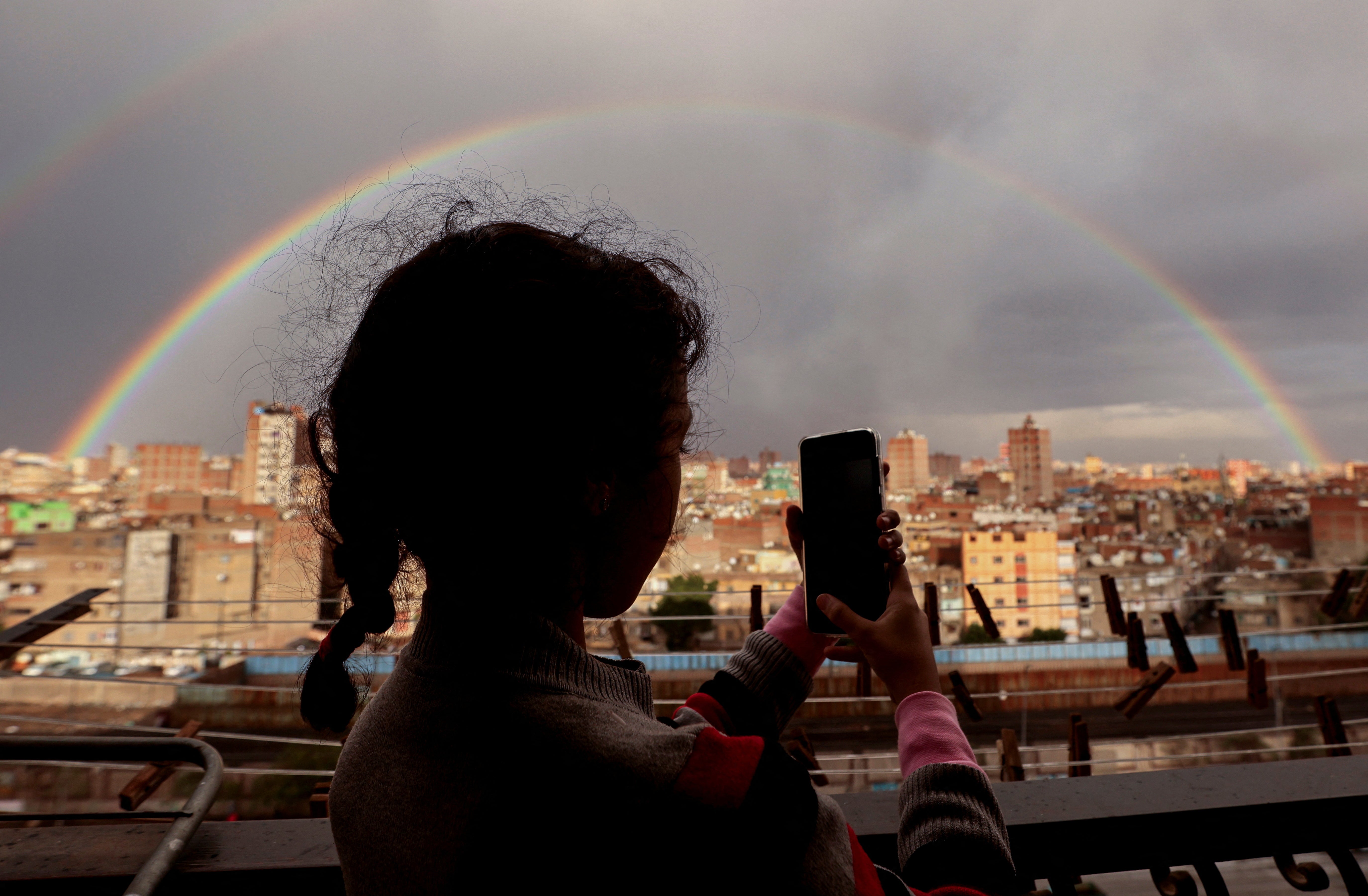 A girl takes a photo of a rainbow in the sky after it rained, in Cairo, Egypt