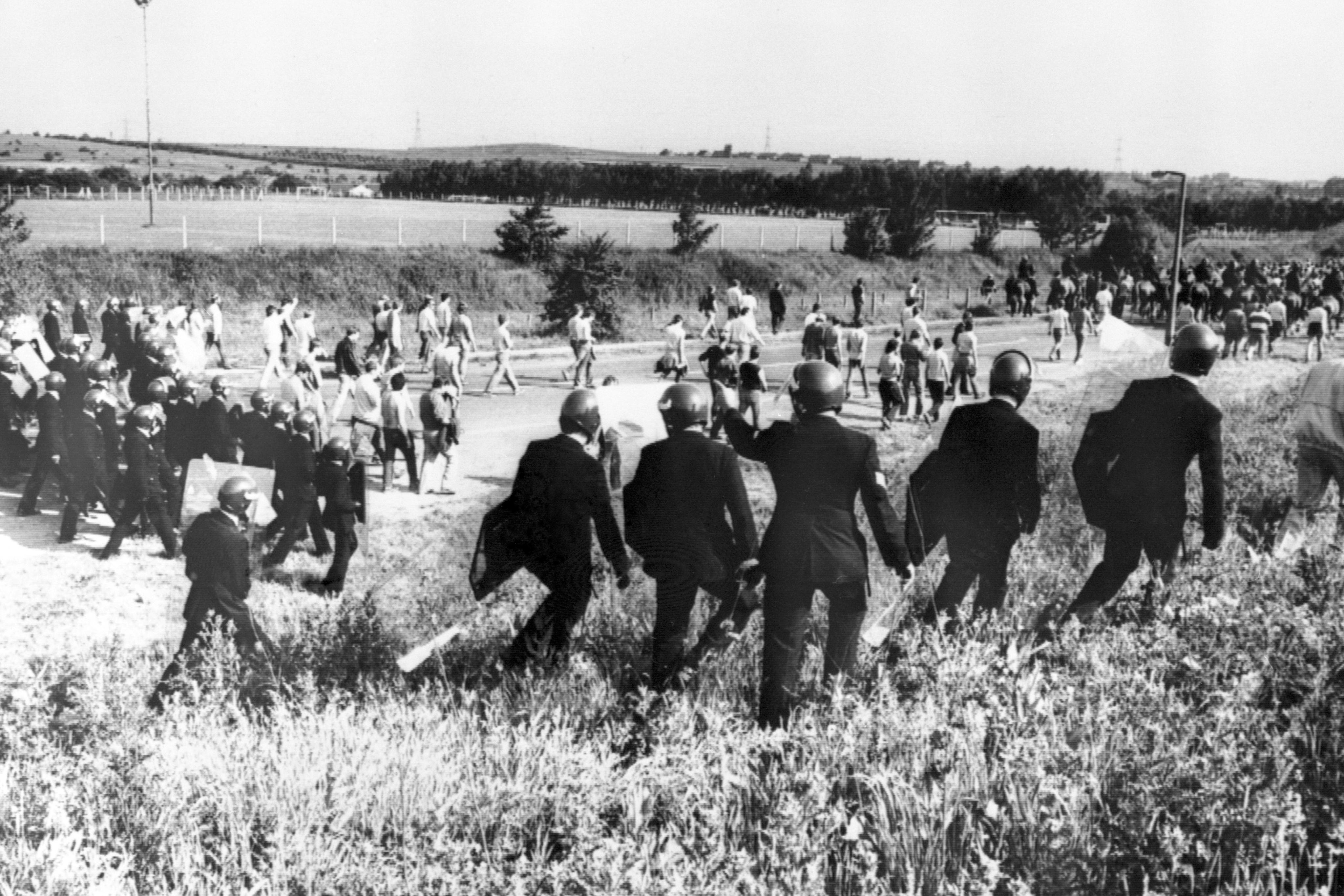 Police in anti-riot gear escort picketers away from their position near the Orgreave coking plant in June 1984 (PA)