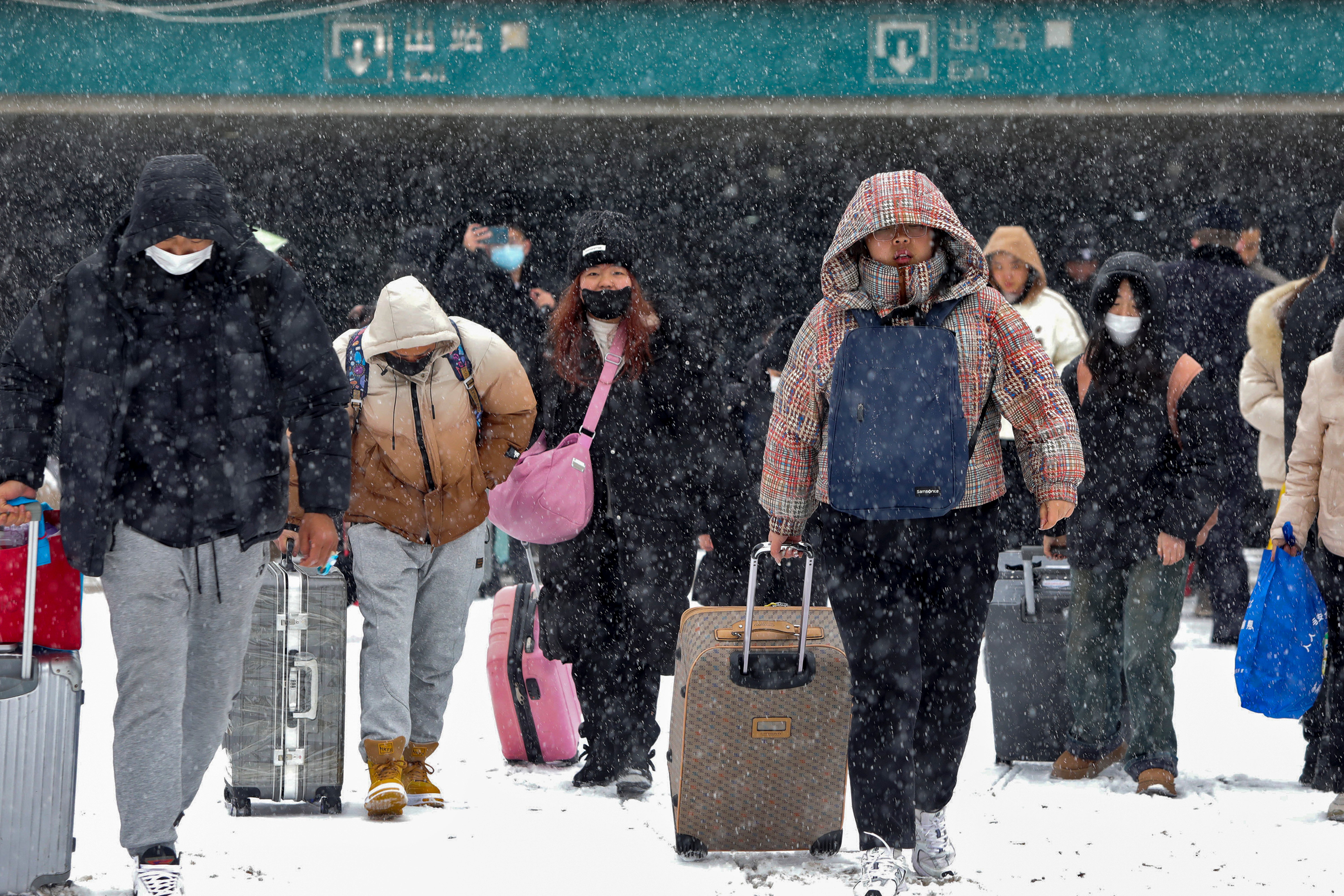 Travellers with their luggage walk in the snow as they exit a railway station in Huaibei, in central China’s Anhui province