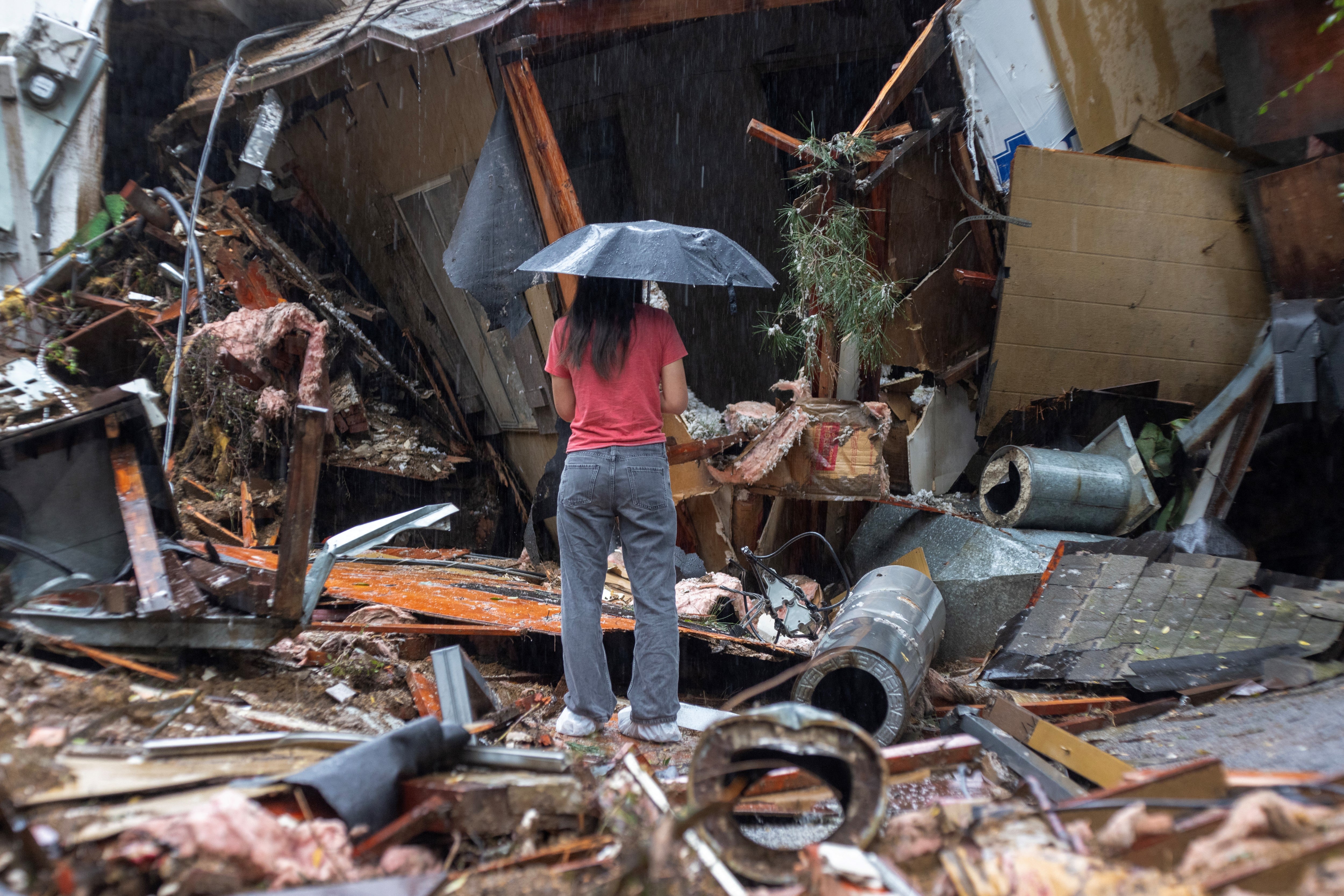 A woman stands among the wreckage of a house that was abruptly destroyed by a landslide as a historic atmospheric river storm inundates the Hollywood Hills area of Los Angeles, California, on February 6,