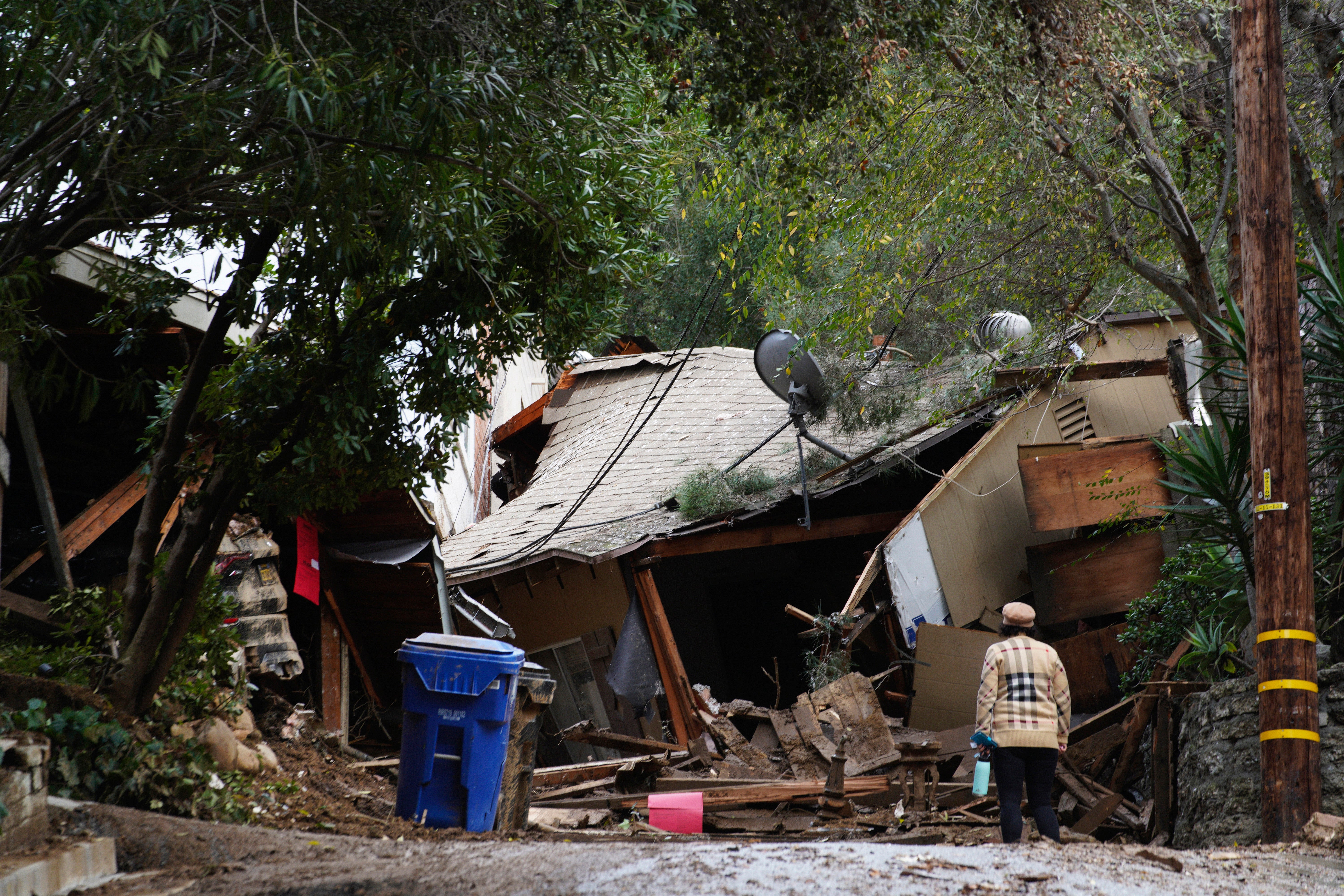 A local resident checks the damage to her neighbor's house after heavy rains and mud flows caused it to slide down from the hill in Beverly Glen