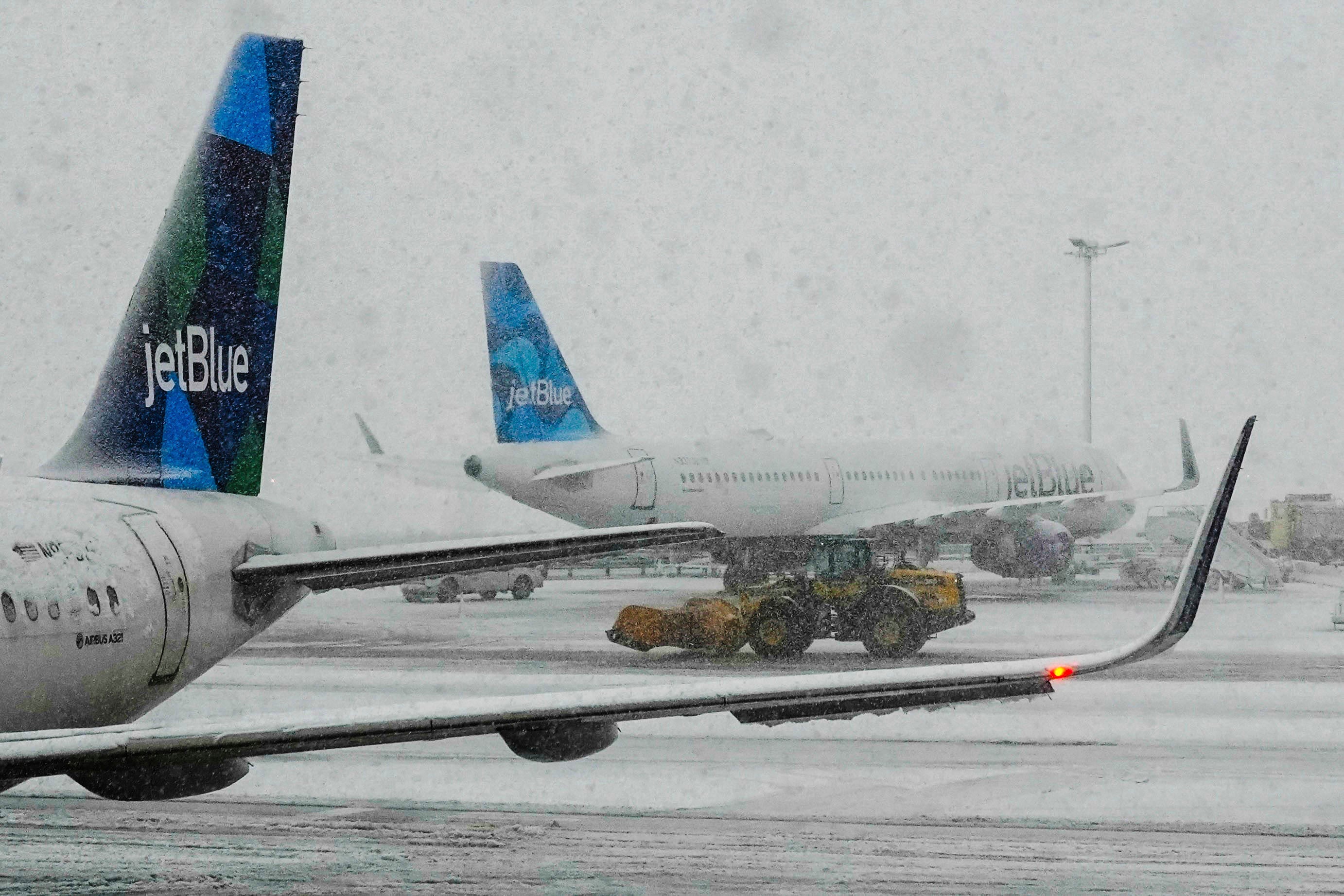 Workers clear the runway near JetBlue planes as snow falls at John F Kennedy International Airport