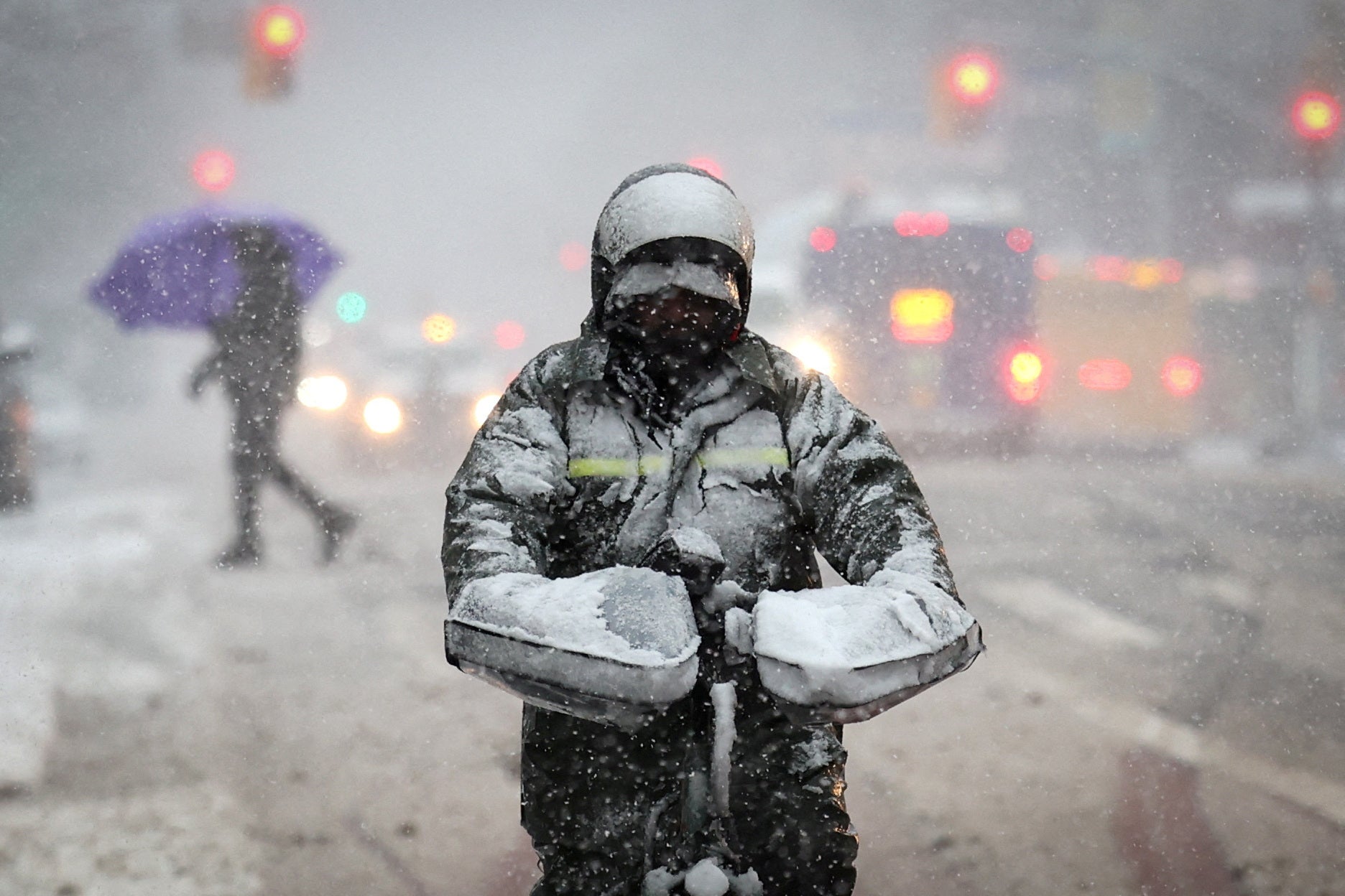 A delivery worker rides a bicycle on East 125th Street in heavy snowfall