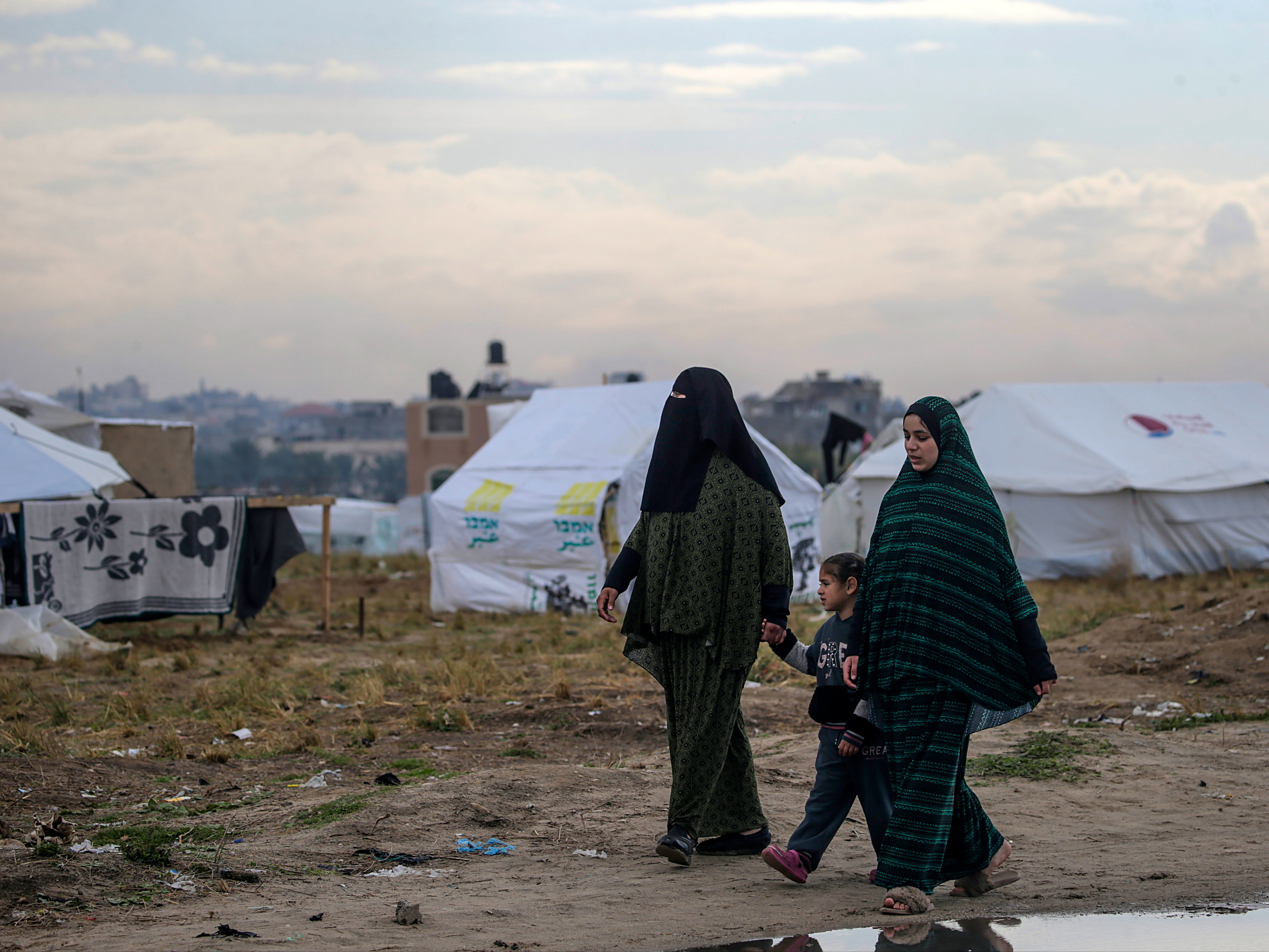 Displaced Palestinian women from Rafah walk next to their shelters in Deir Al Balah, southern Gaza