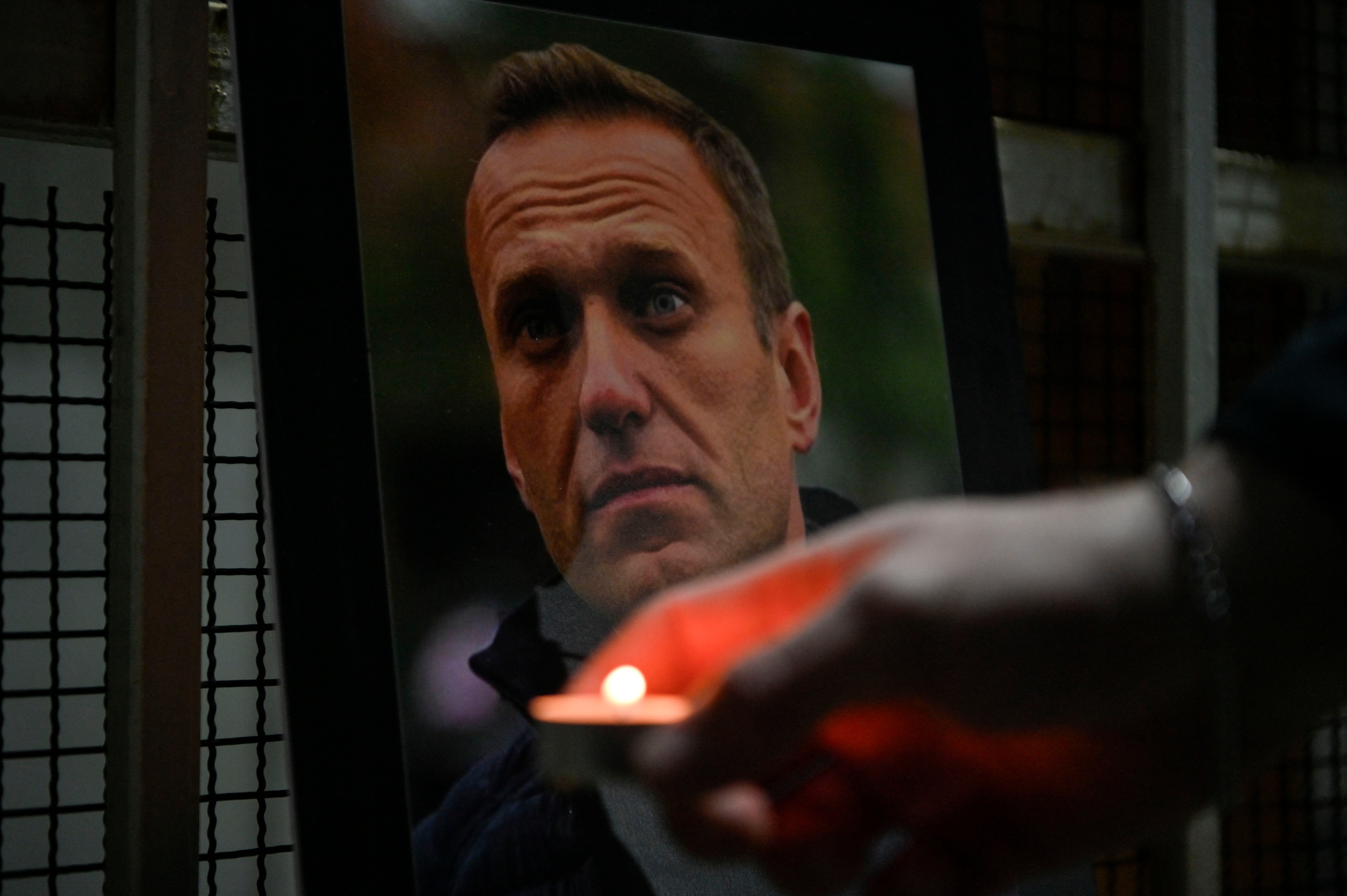 A person lights a candle by a portrait of late Russian opposition leader Alexei Navalny, who died in a Russian Arctic prison, placed at the entrance of the Chancery of the Embassy of the Russian Federation in Pristina on 20 February 2024