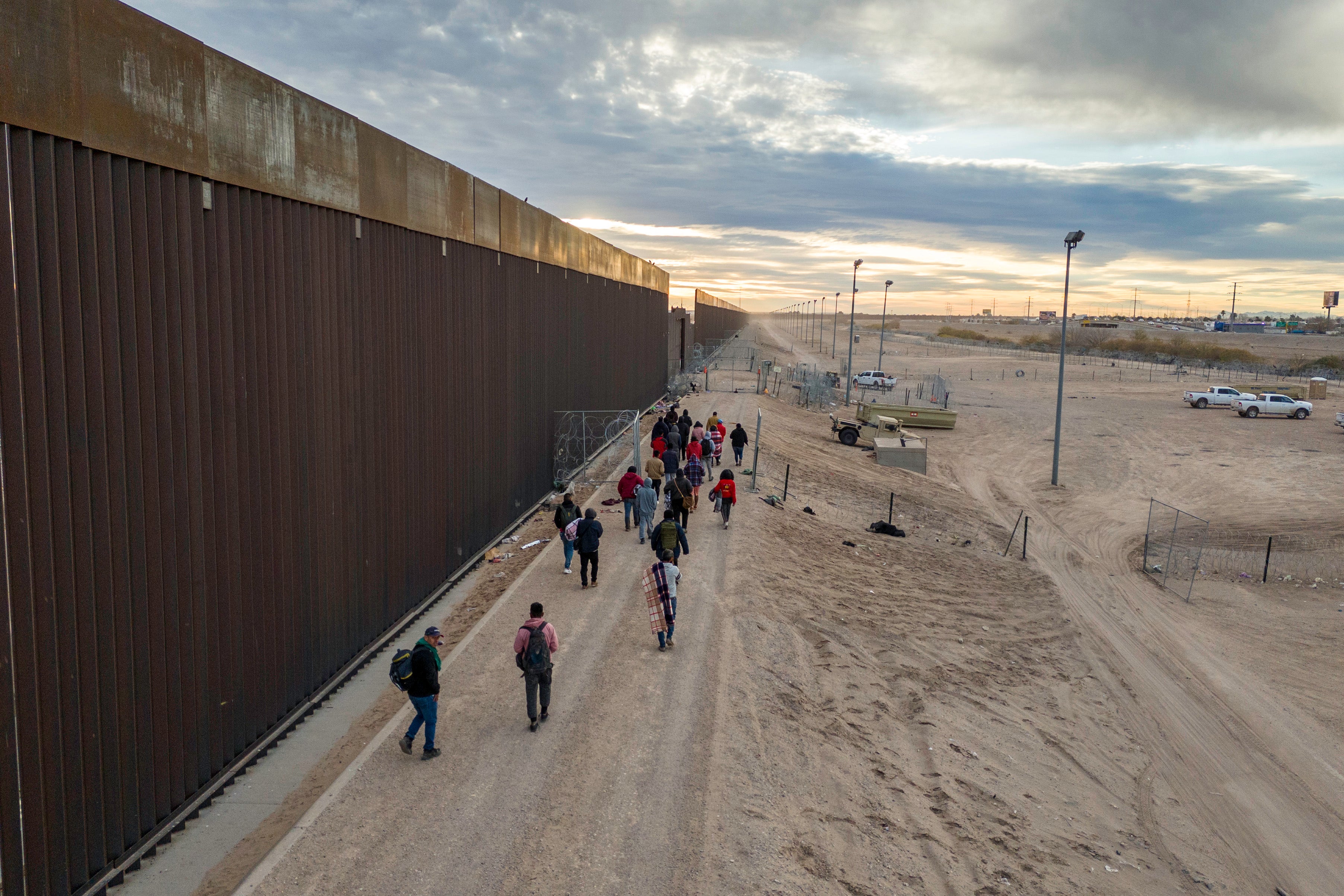 Seen from an aerial view, immigrants walk along the U.S.-Mexico border wall after crossing the Rio Grande into El Paso, Texas on 1 February 2024 from Ciudad Juarez, Mexico