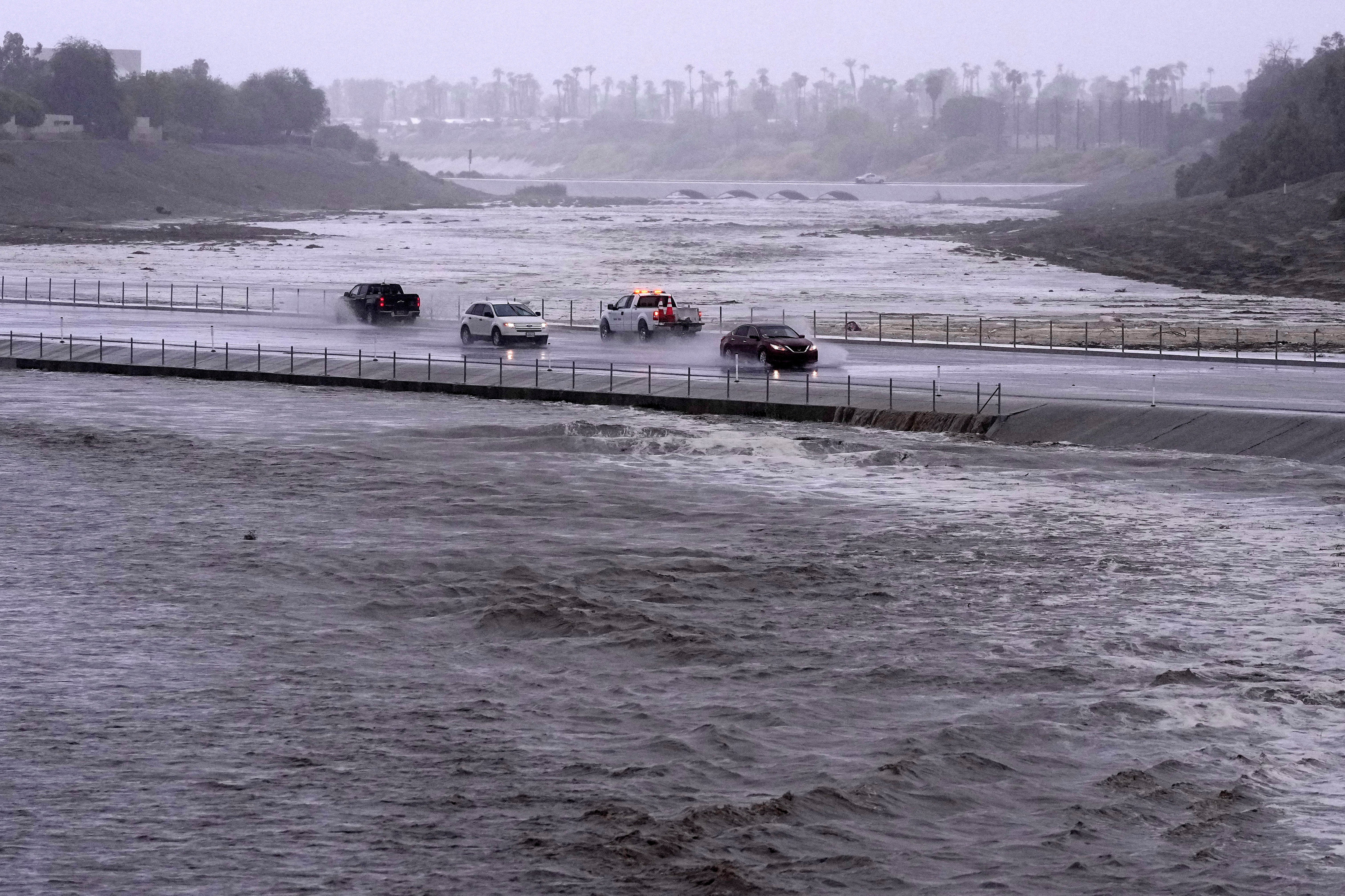 Vehicles cross over a flood control basin that has almost reached the street as Tropical Storm Hilary hits the area on Aug. 20, 2023, in Palm Desert, Calif.