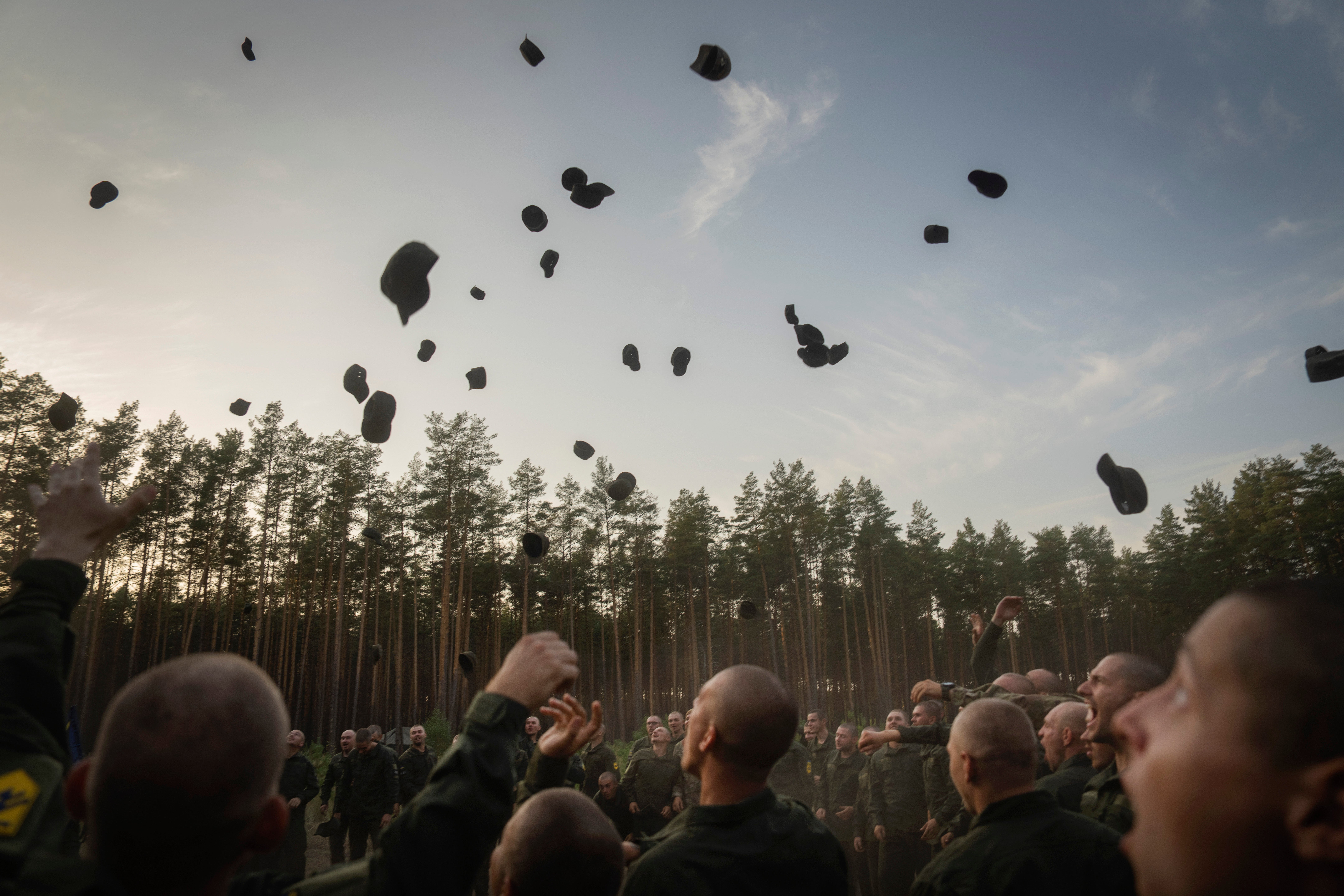 Newly recruited soldiers toss their hats as they celebrate the end of their training at a military base close to Kyiv