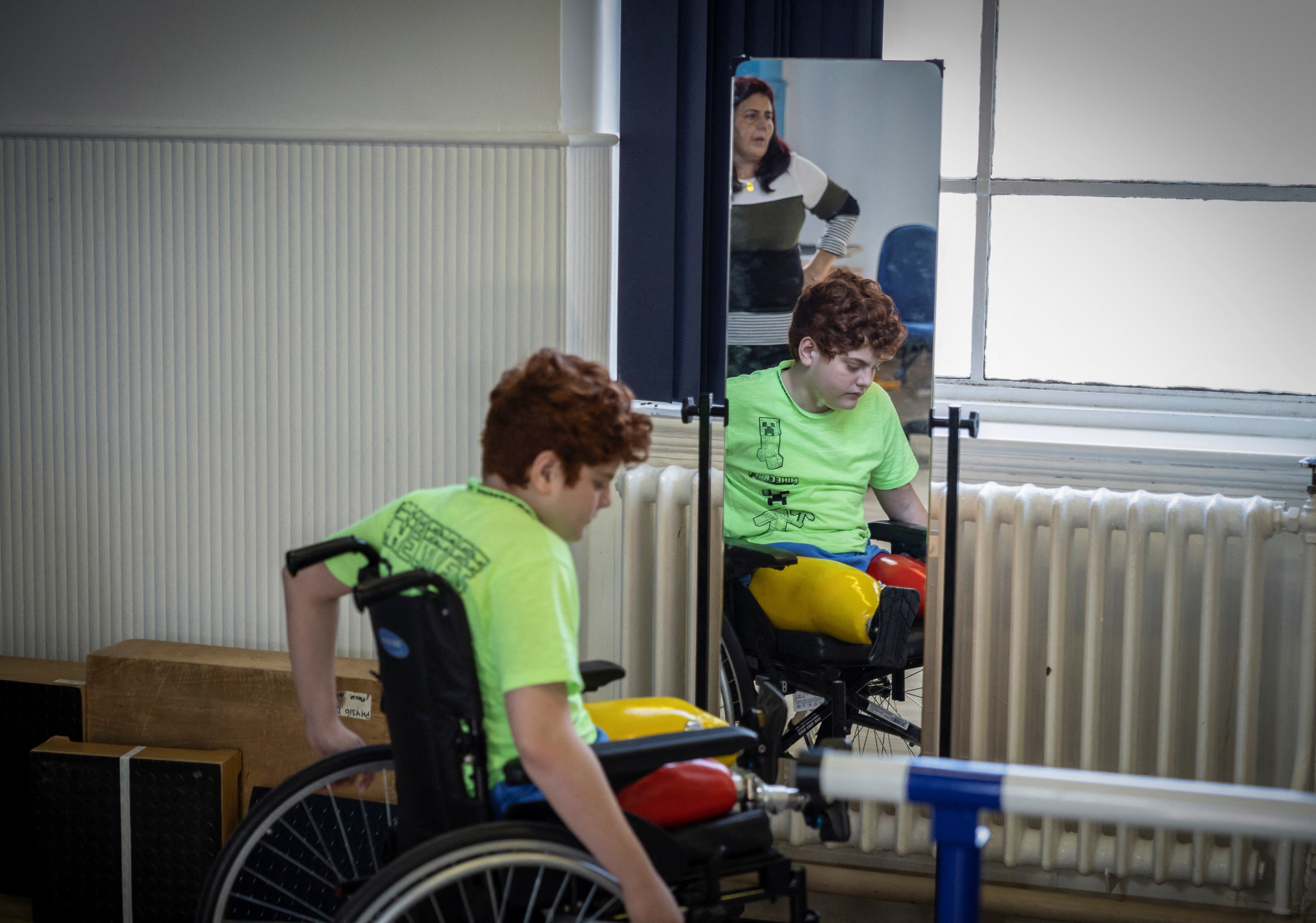 Mehmet, uses his wheelchair ahead of using physiotherapy bars, as his translator looks on