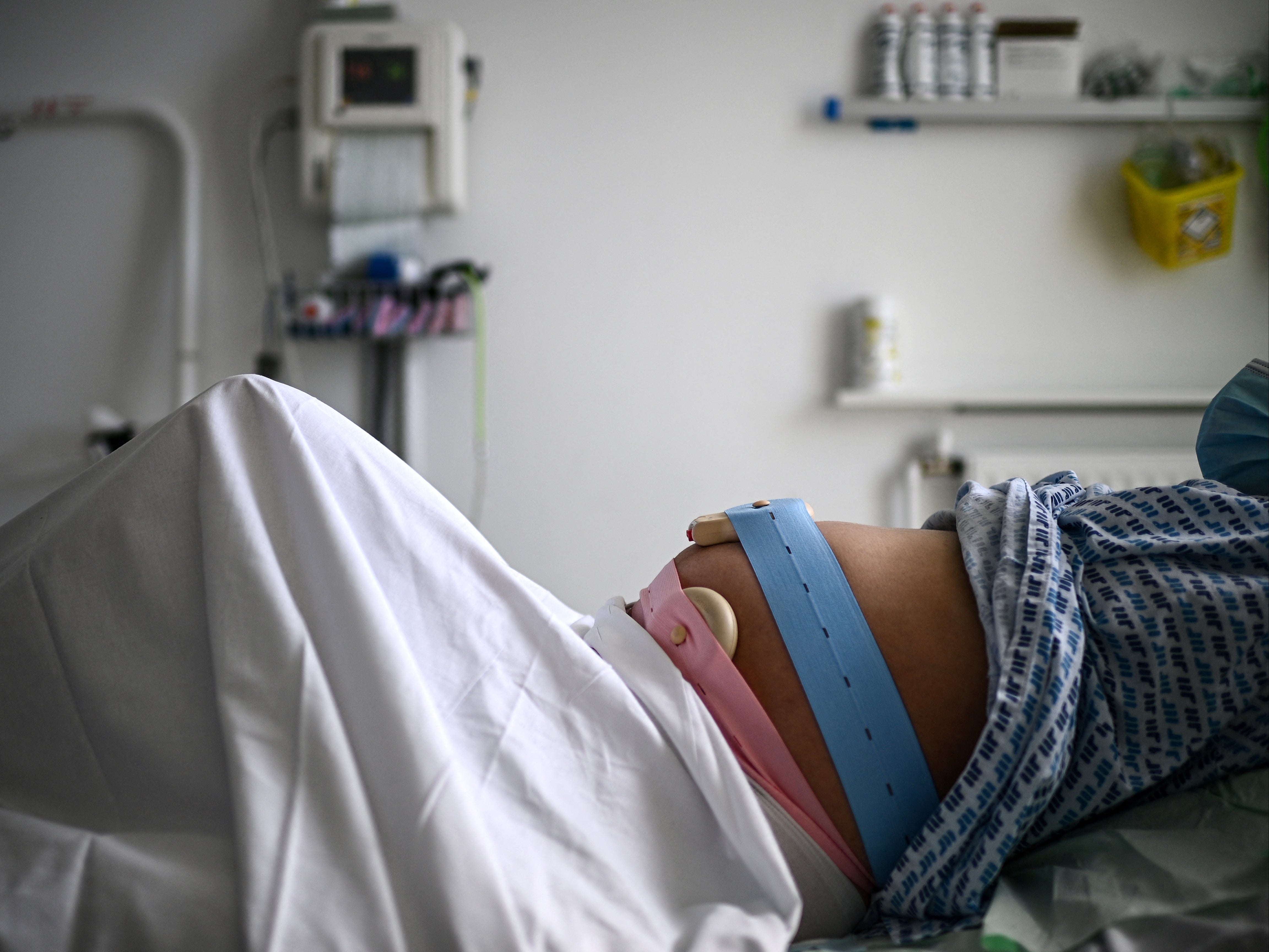 A pregnant woman lies on her bed with monitoring devices placed on her belly as she gets ready before delivering her child at the maternity ward of a hospital in Paris on June 29, 2022