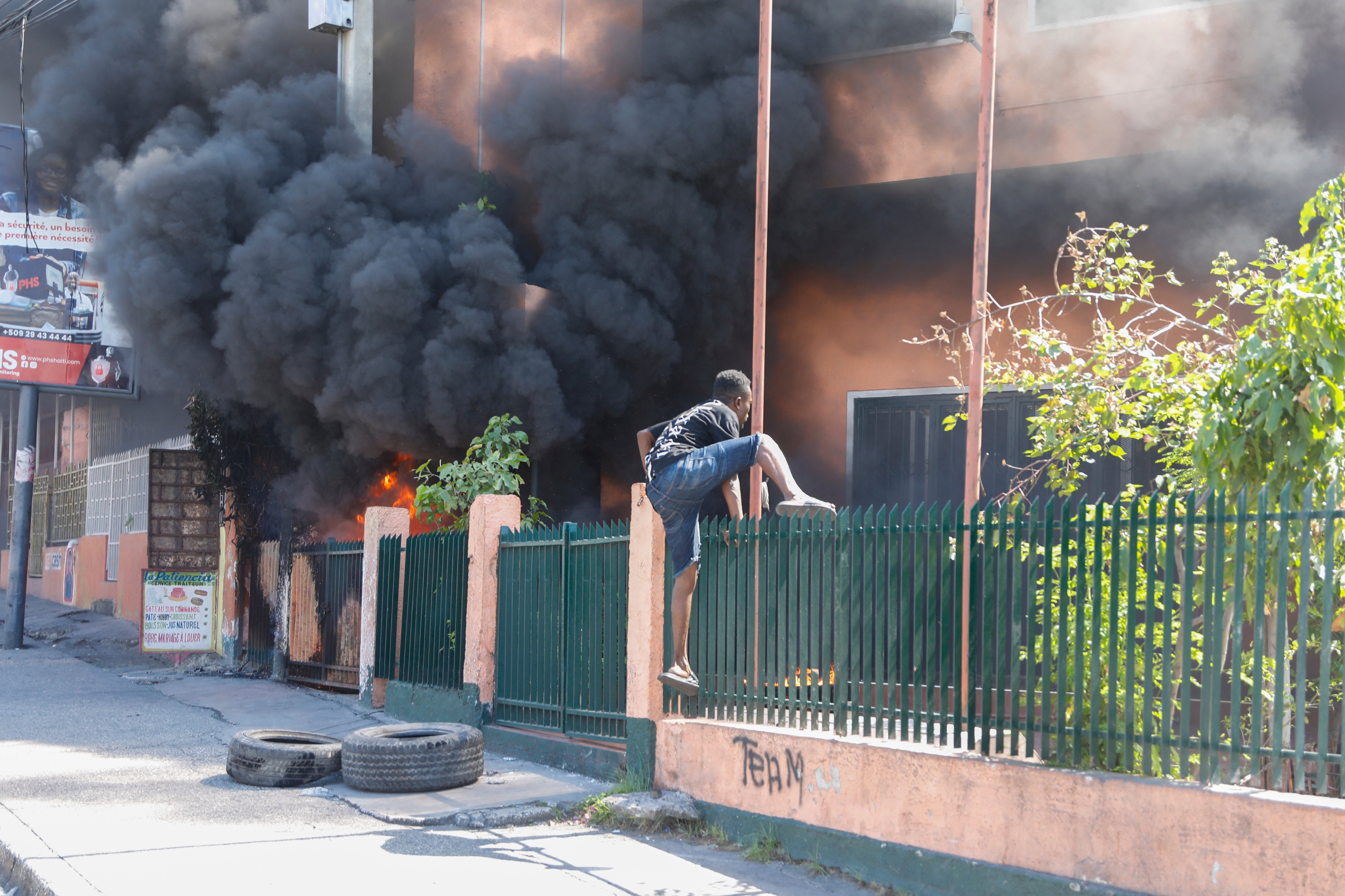 A man climbs the fence of an office of Haiti’s power company set on fire during a protest