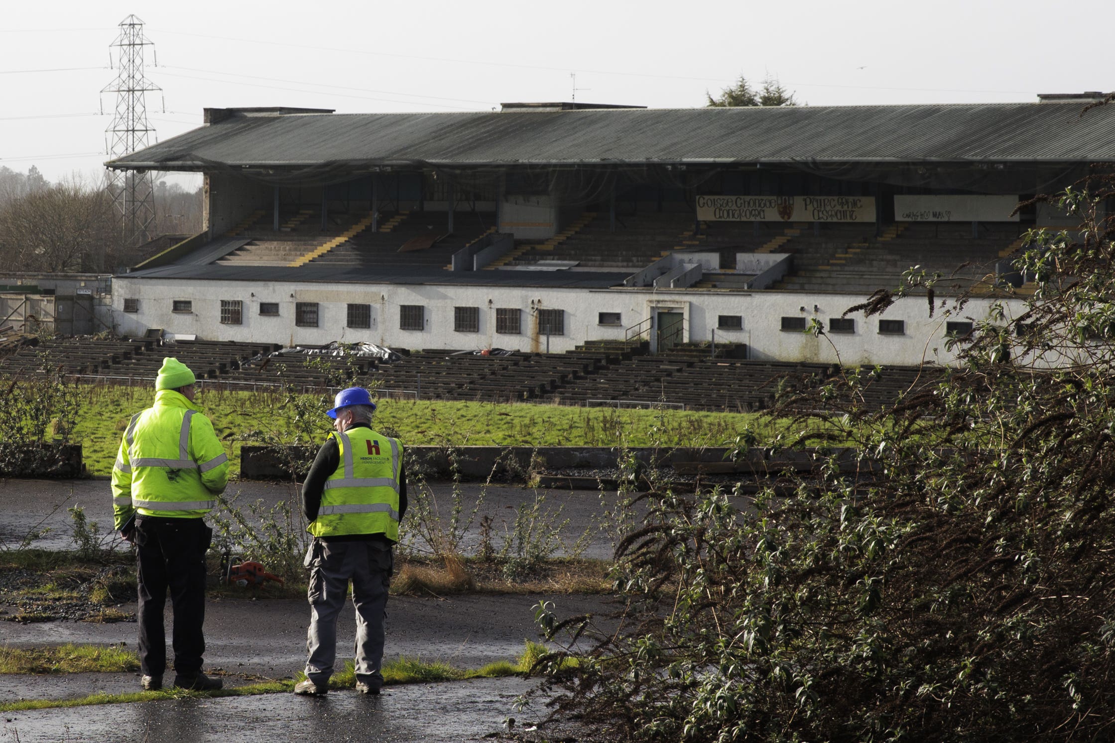 Workmen at Casement Park GAA stadium in Belfast, Northern Ireland. Contractors have begun assessing planned ground works at Casement Park ahead of the long-delayed redevelopment of the stadium.The maintenance and pre-enabling works will run until April, when the demolition of the existing terraces will begin. The GAA is undertaking the initial phase of works amid continued uncertainty over the funding of the redevelopment. The stadium in west Belfast has been earmarked for matches at the Euro 2028 football tournament and will need to be completed well in advance of that event to be rubber-stamped as an approved venue. Picture date: Monday February 19, 2024.