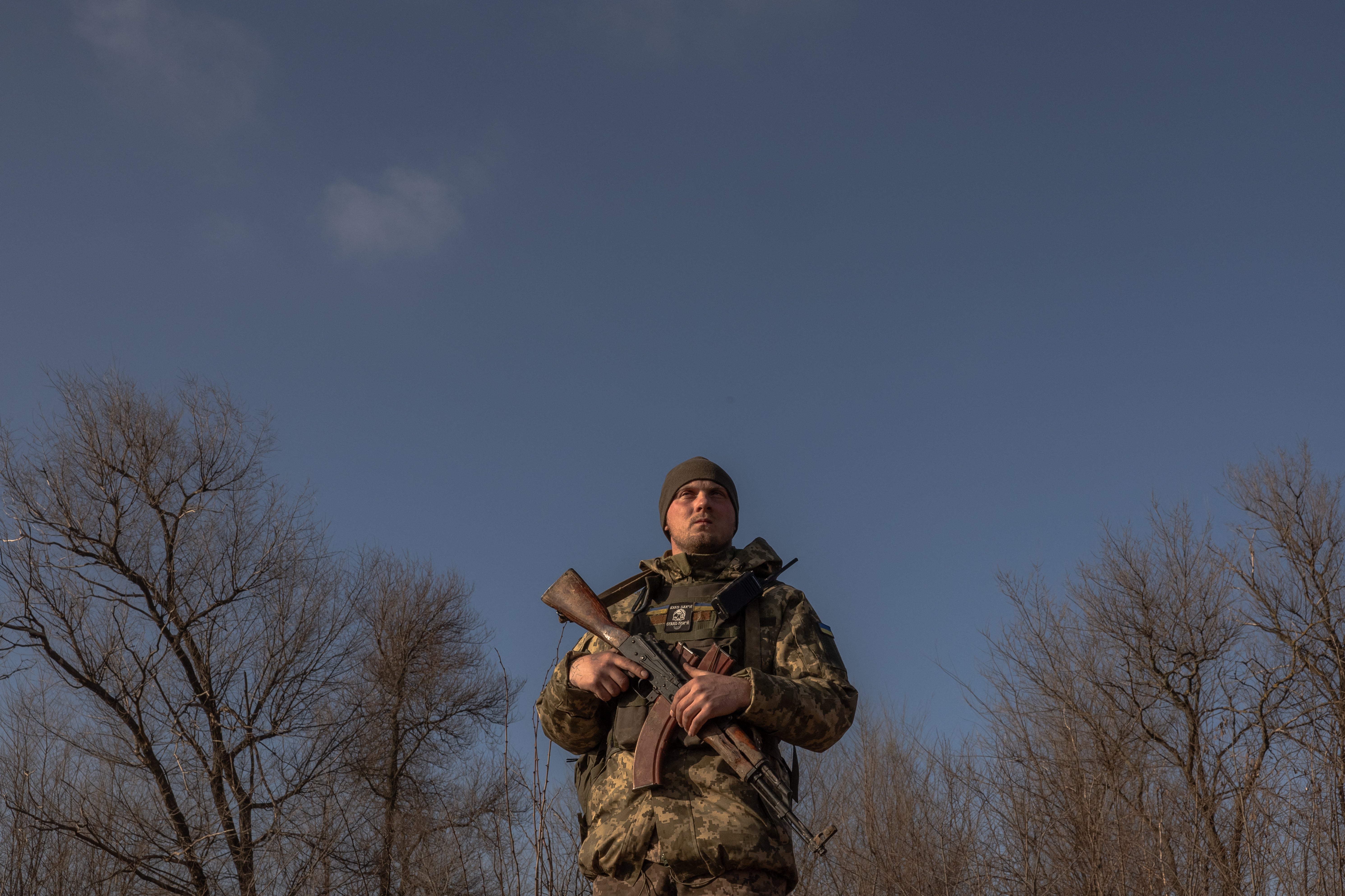 A Ukrainian serviceman stands guard checking for Russian drones in the sky as a soldier in a tractor digs a trench system in the Zaporizhzhia region in January