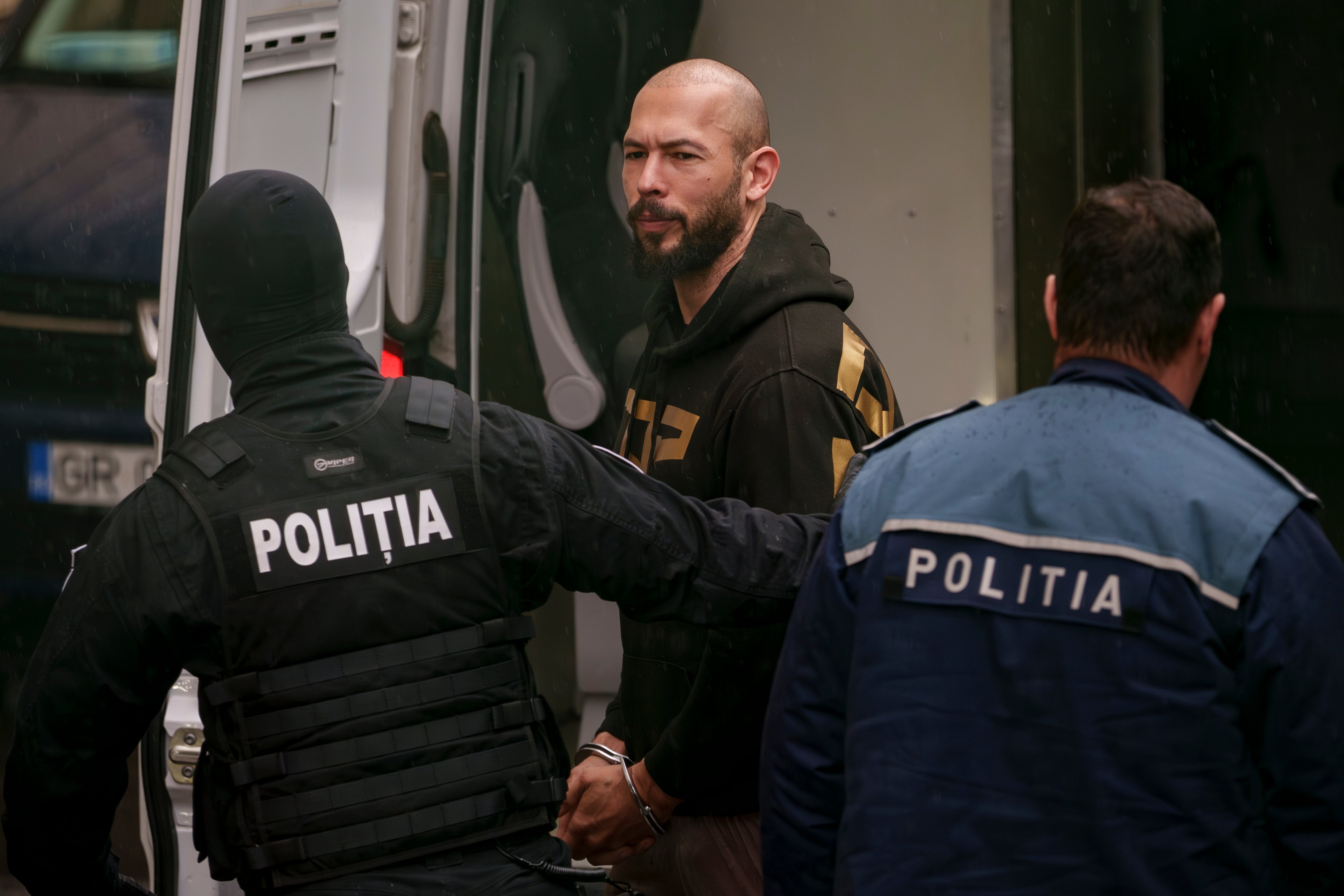 Police officers escort Andrew Tate, center, handcuffed, to the Court of Appeal in Bucharest, Romania, Tuesday, March 12